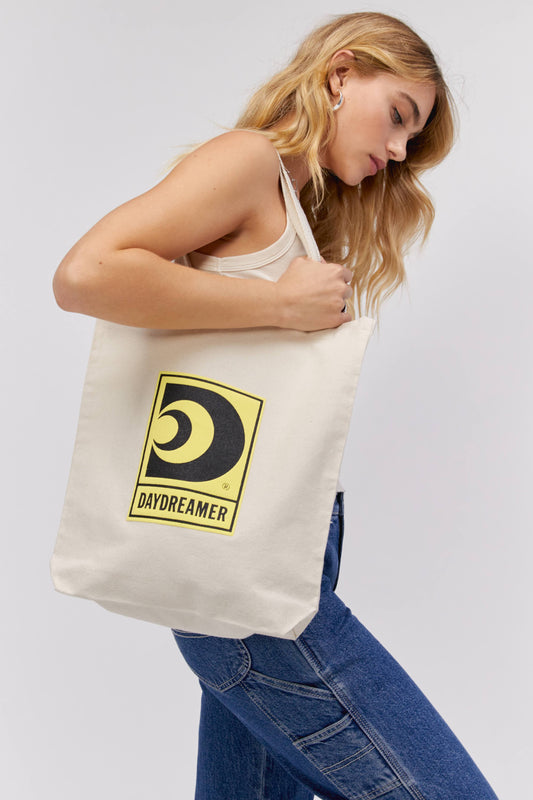 GIRL HOLDING CANVAS TOTE WITH YELLOW DAYDREAMER LOGO