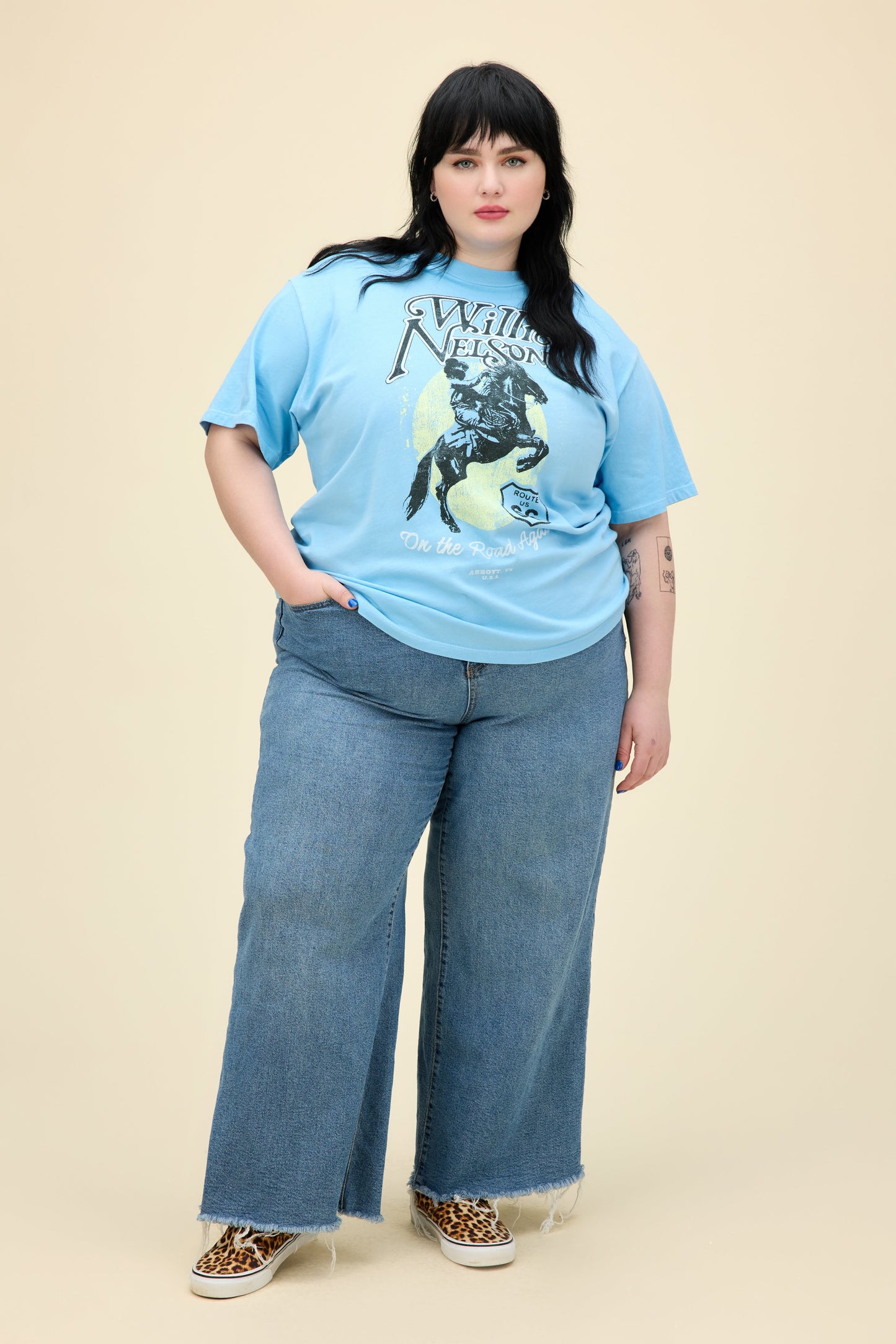 A model featuring a blue plus size weekend tee stamped with Willie Nelson and his route 66 album cover.