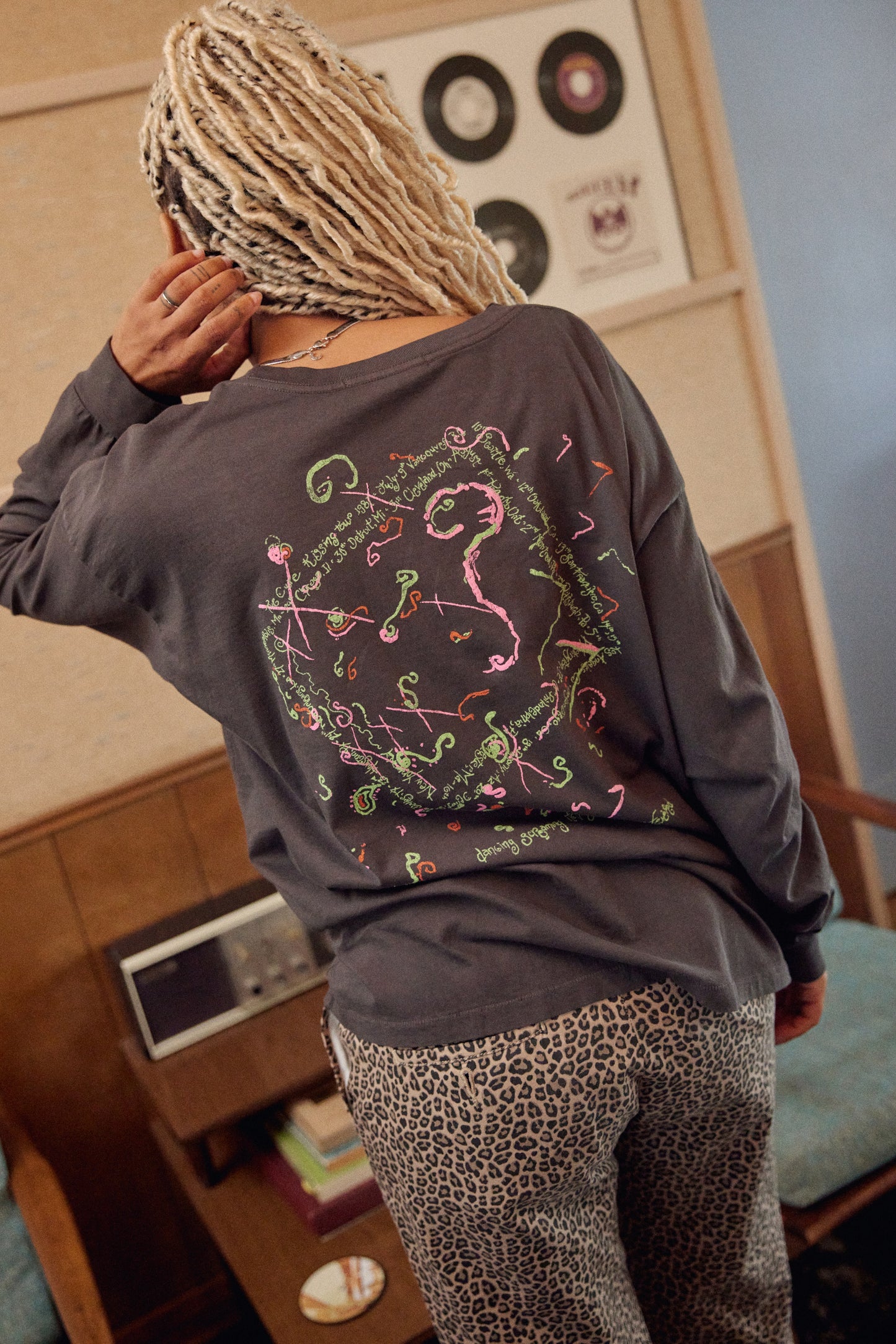A model featuring a black The Cure long sleeve merch designed with a hand-drawn portrait of Smith and doodles in puff ink and pops of color.