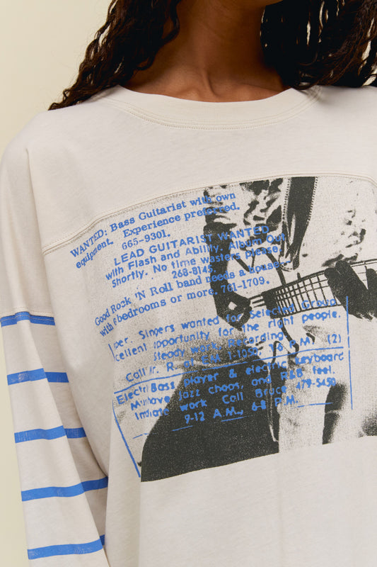 A  dark-haired model wearing dirty white long sleeves featuring a graphic art of a guitarist. 
