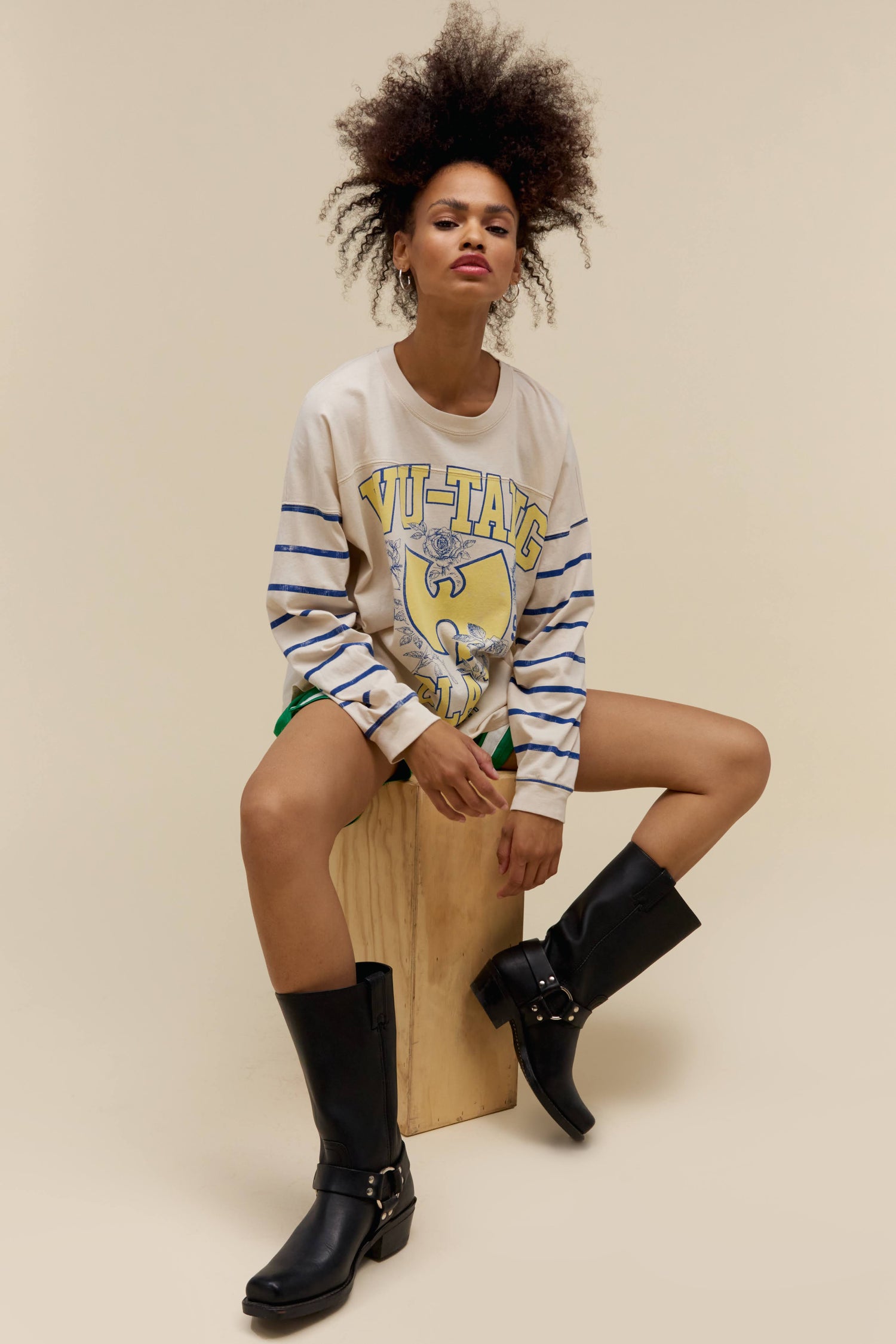 A model featuring a white varsity long sleeve stamped with Wu-tang Clan in large yellow font and their logo.