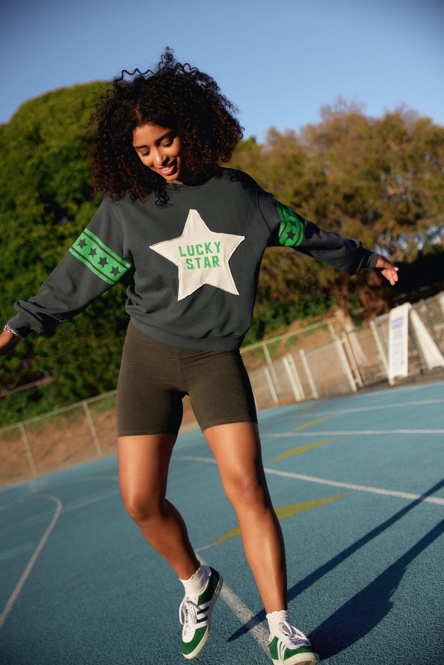 A model featuring a black sweatshirt designed with a  large star in the middle, stamped with "Lucky Star" and green stripes on the sleeves.