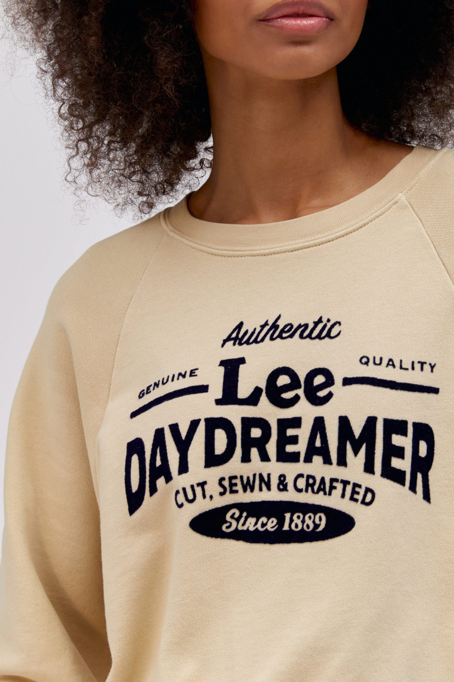 close up detail photo of model wearing a khaki colored sweatshirt with flocked logo graphics