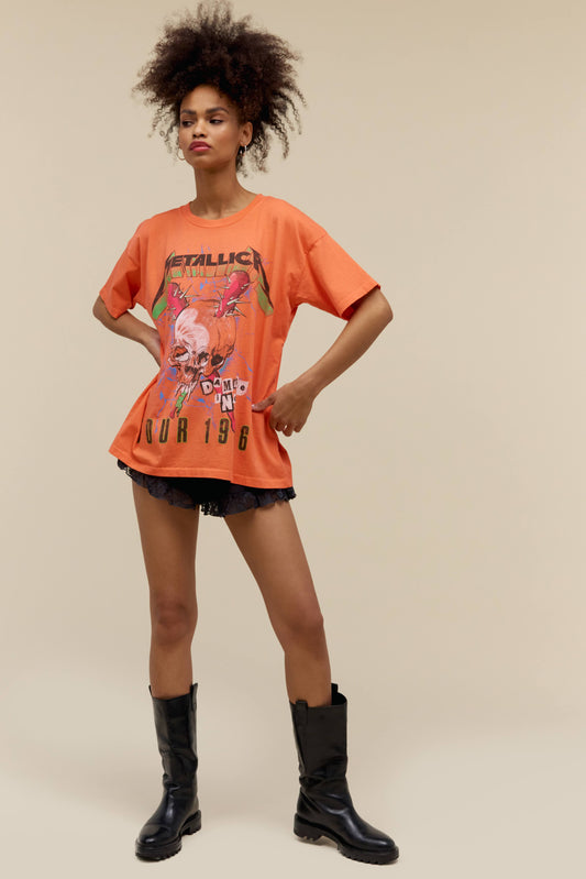 A model featuring an orange merch tee stamped with Metallica and a graphic skull on the middle.