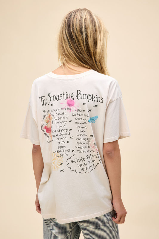 A model featuring a white merch tee stamped with 'The Smashing Pumpkins' and a bunch of angels, statues, and flowers around.