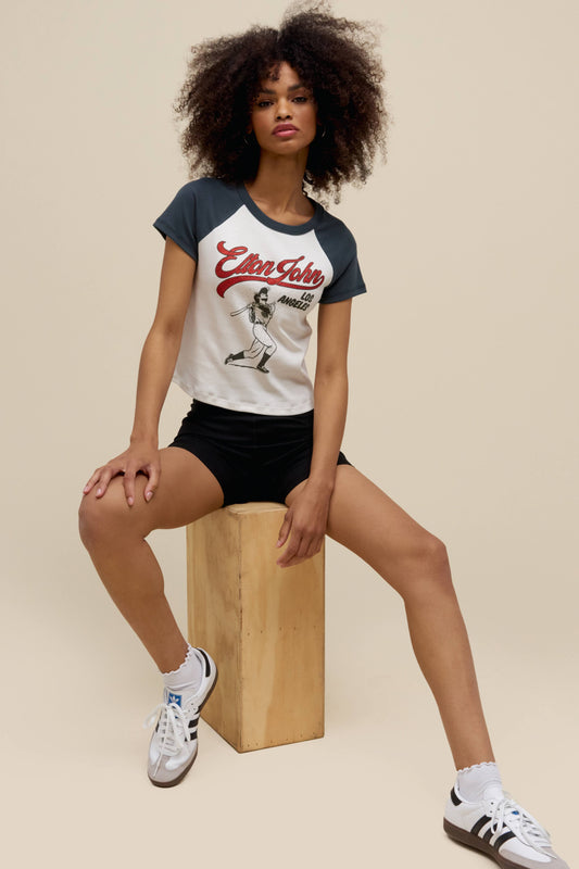 A model featuring a black and white shrunken raglan stamped with a graphic icon of Elton John on the center.