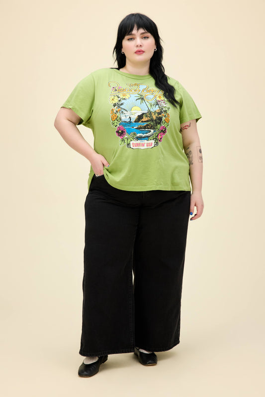 A model featuring a plus size matcha ringer tee stamped with 'The Beach Boys', with their graphic beach logo.