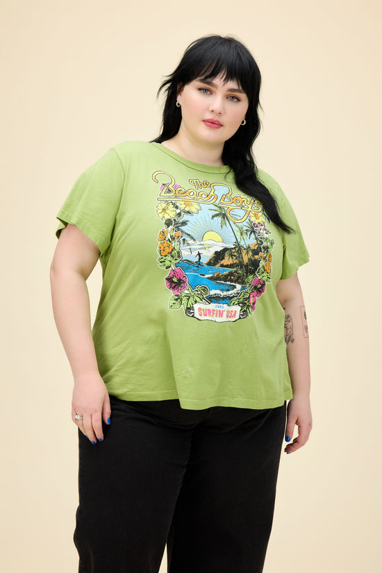 A model featuring a plus size matcha ringer tee stamped with 'The Beach Boys', with their graphic beach logo.