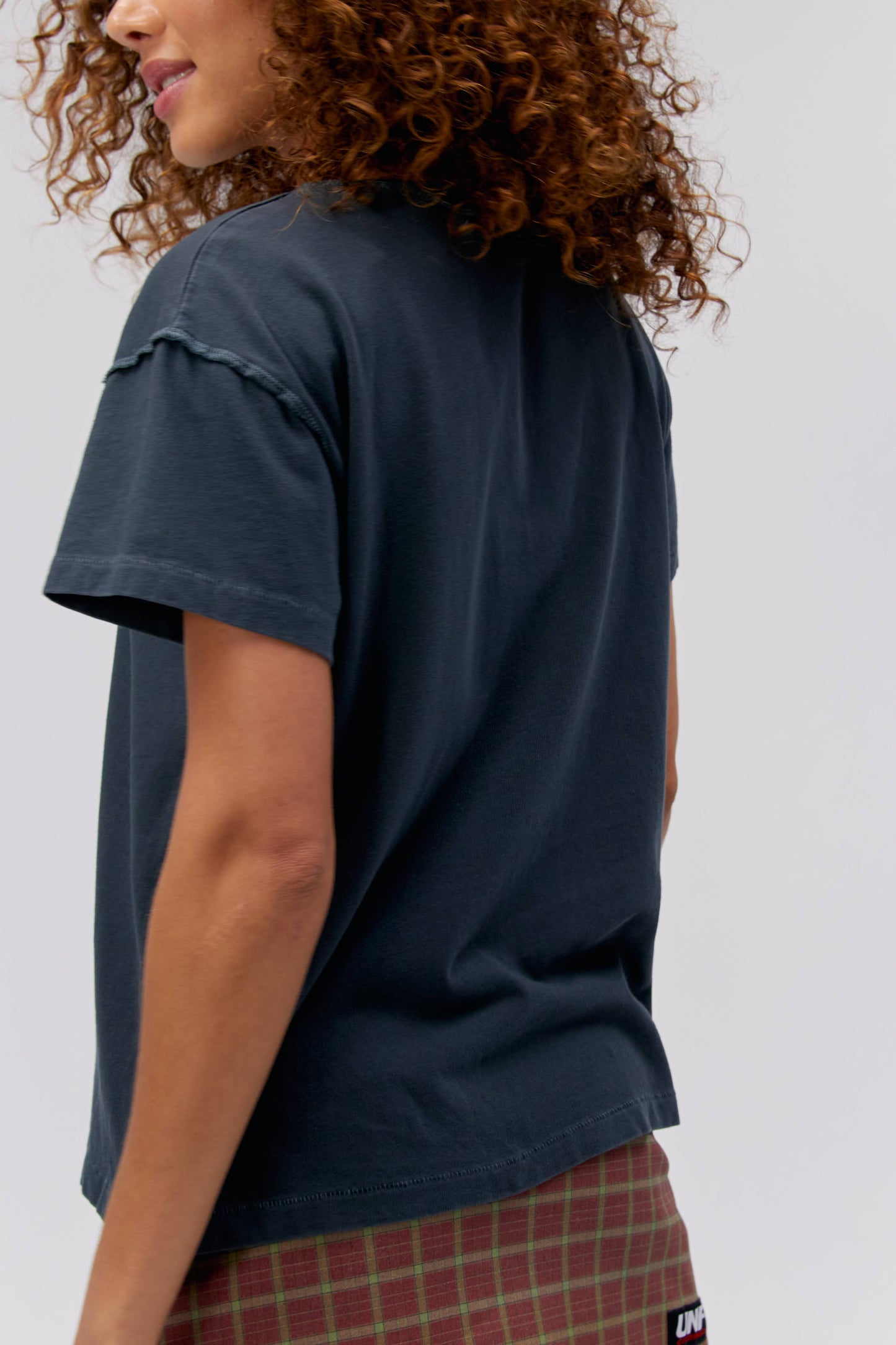 A curly-haired model featuring a black tee stamped with 'Billy Joel' in blue, green, and yellow gradient letters, along with a portrait of the artist in the center.