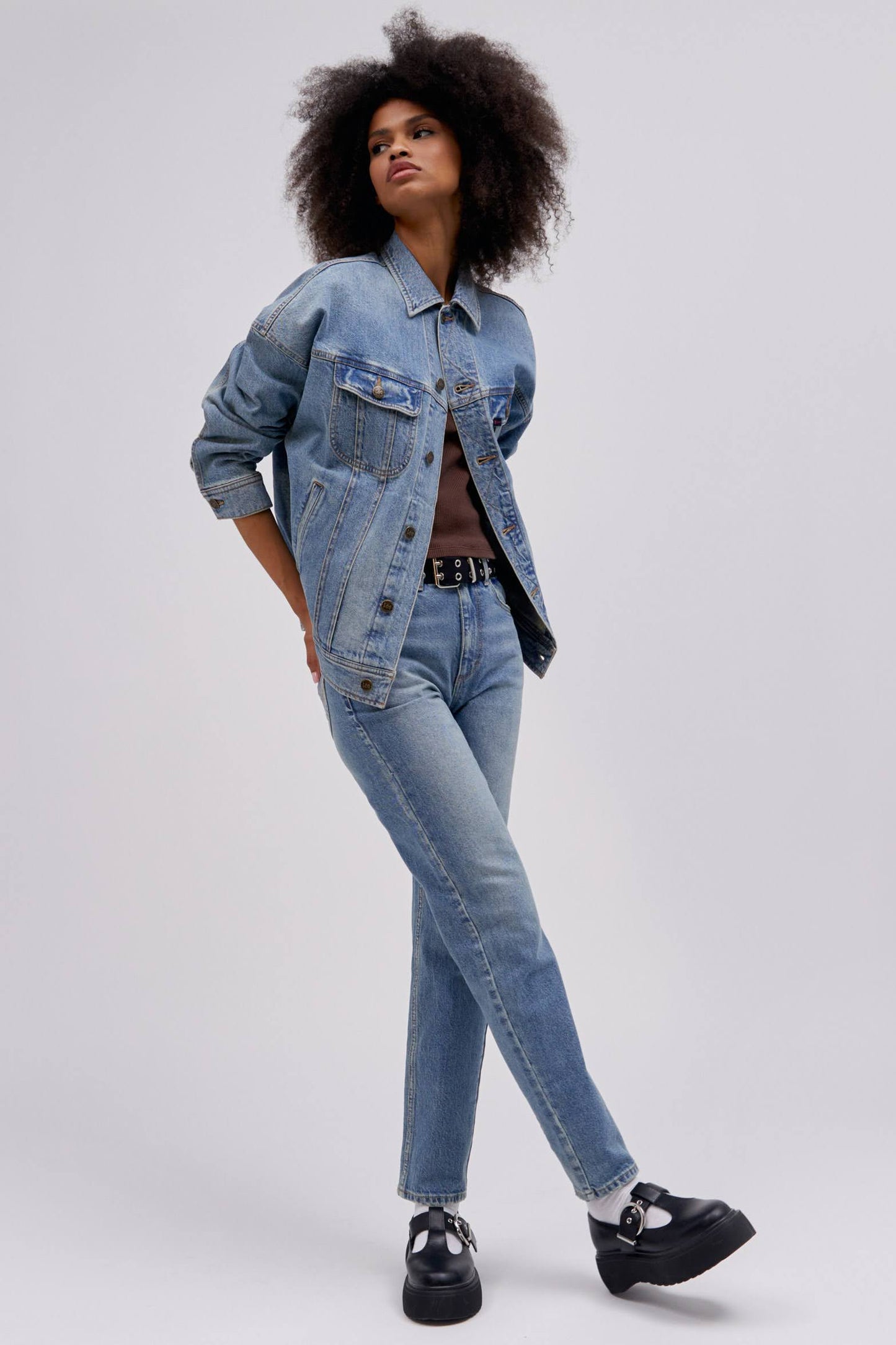 Curly haired model posing and wearing a reimagined Lee Denim rider jacket in an oversized fit.
