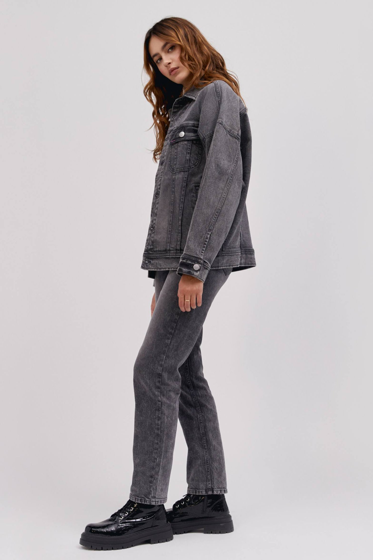 A curly-haired model featuring a sharp turn colored Loose Rider Jacket with a set of vertical pleats to the iconic zig-zag stitching and designed with an oversized look.
