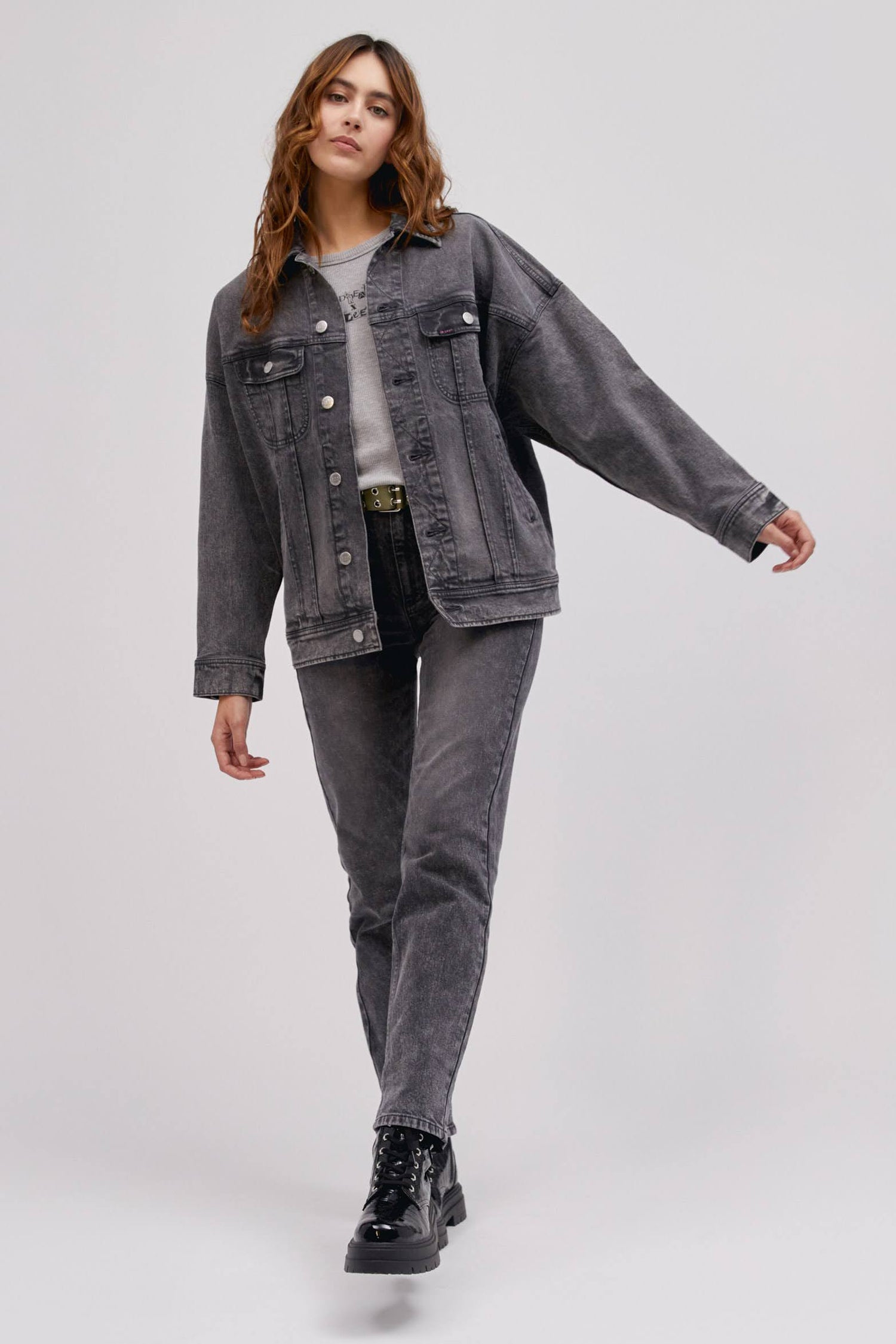 A curly-haired model featuring a sharp turn colored Loose Rider Jacket with a set of vertical pleats to the iconic zig-zag stitching and designed with an oversized look.