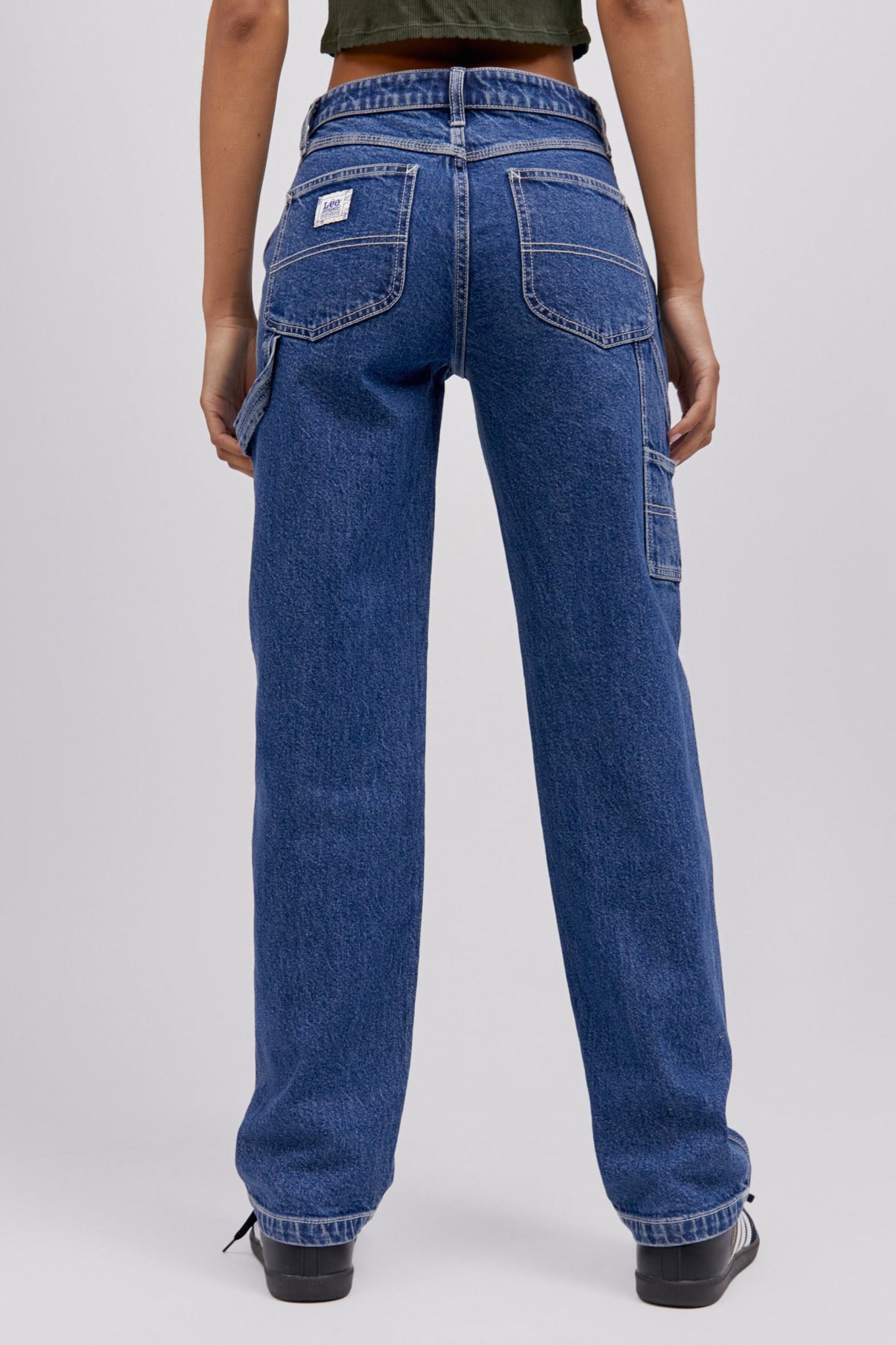 A  model featuring a blue workwear pant made from heavy cotton, accented with key Lee detailing of triple-stitched seams, oversized pockets and a uniform like hammer loop.