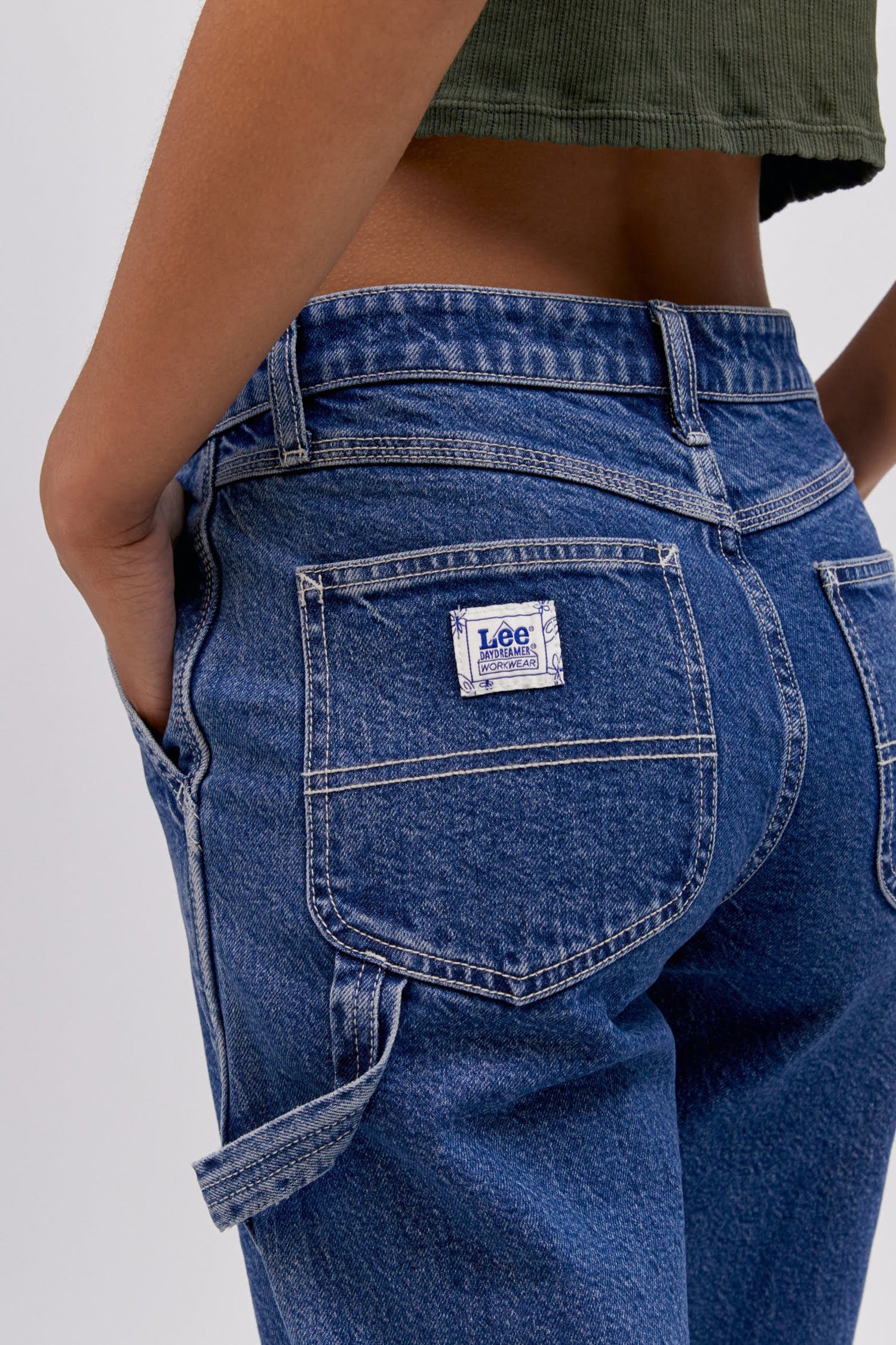 A  model featuring a blue workwear pant made from heavy cotton, accented with key Lee detailing of triple-stitched seams, oversized pockets and a uniform like hammer loop.