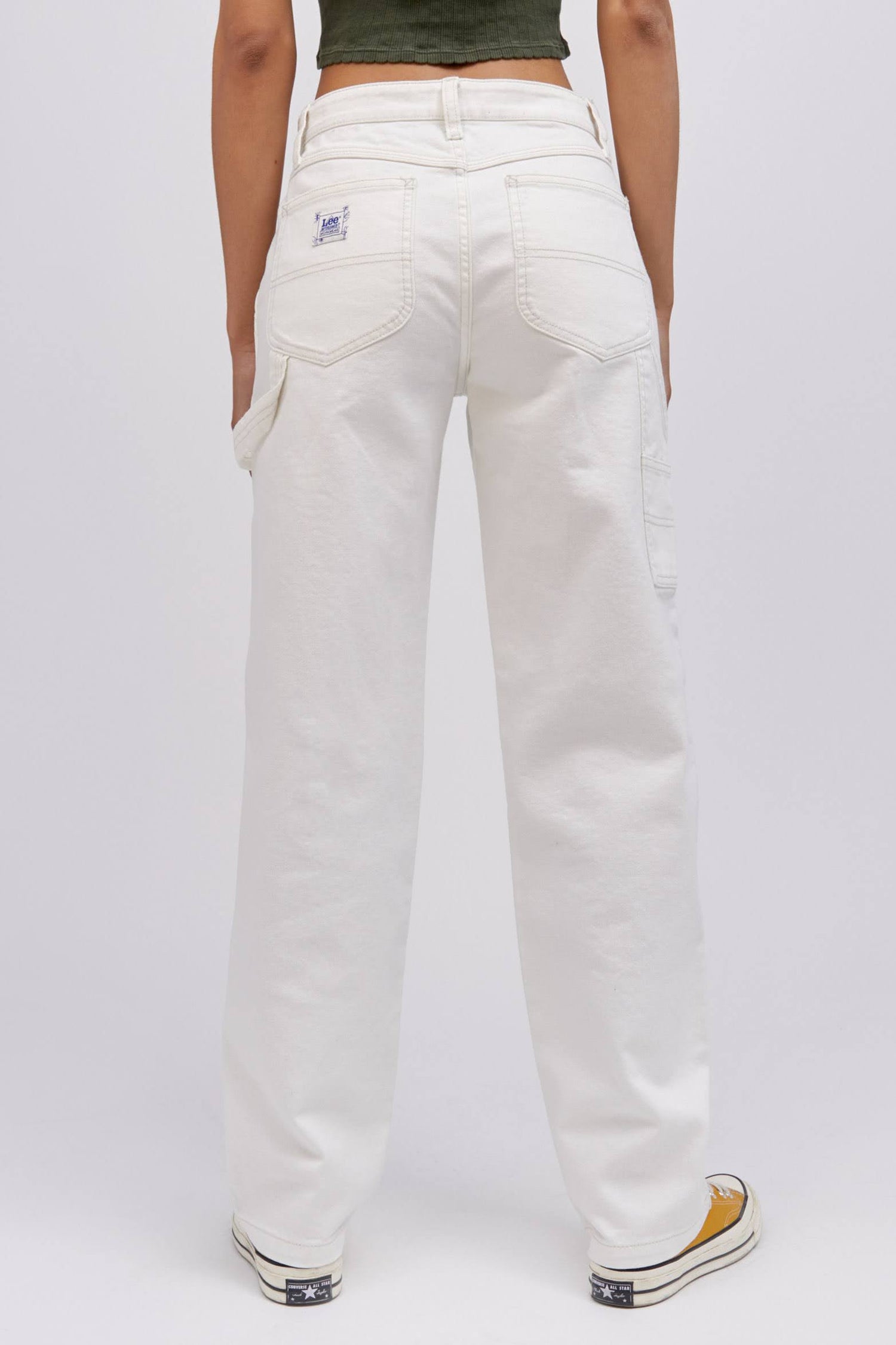 A  model featuring a white workwear pant made from heavy cotton, accented with key Lee detailing of triple-stitched seams, oversized pockets and a uniform like hammer loop.