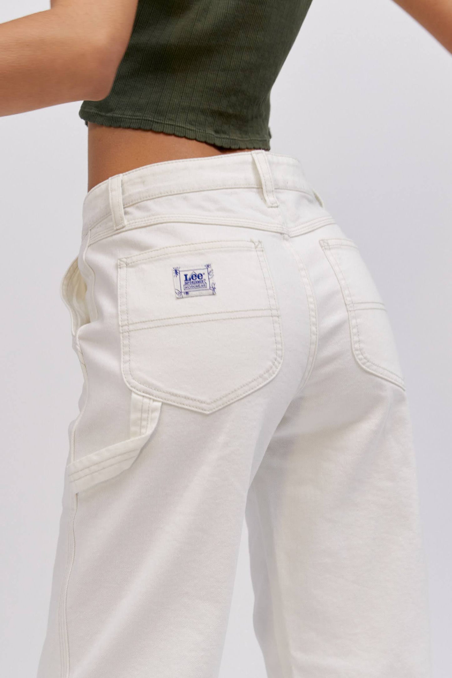 A  model featuring a white workwear pant made from heavy cotton, accented with key Lee detailing of triple-stitched seams, oversized pockets and a uniform like hammer loop.