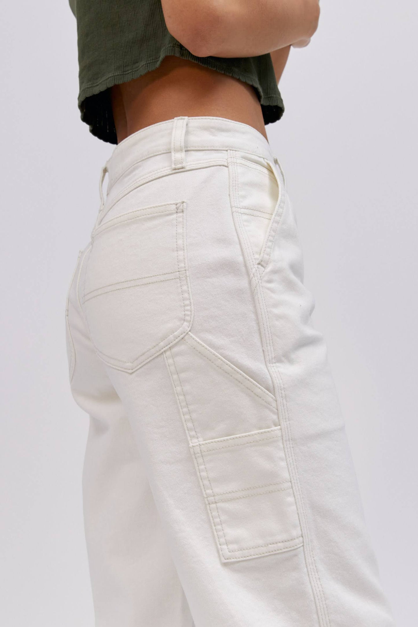 A  model featuring a white workwear pant made from heavy cotton, accented with key Lee detailing of triple-stitched seams, oversized pockets and a uniform like hammer loop.