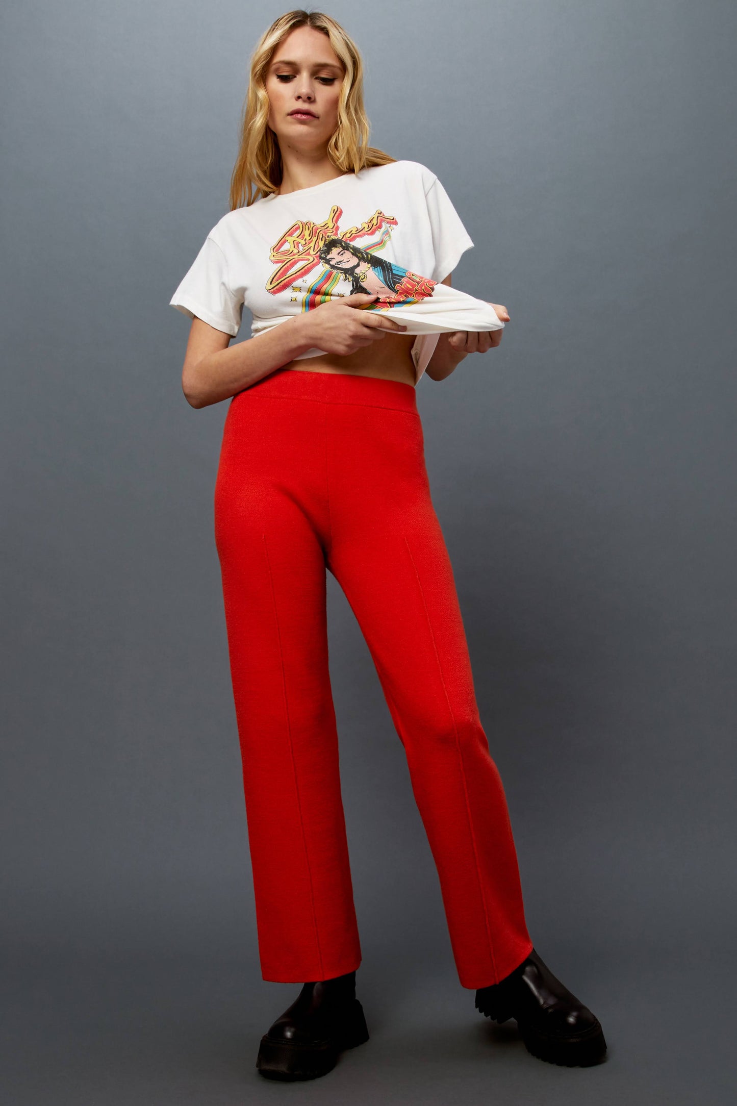 Model wearing a pair of knit pintuck pants in hot orange styled with a Rod Stewart rainbow artwork graphic tee