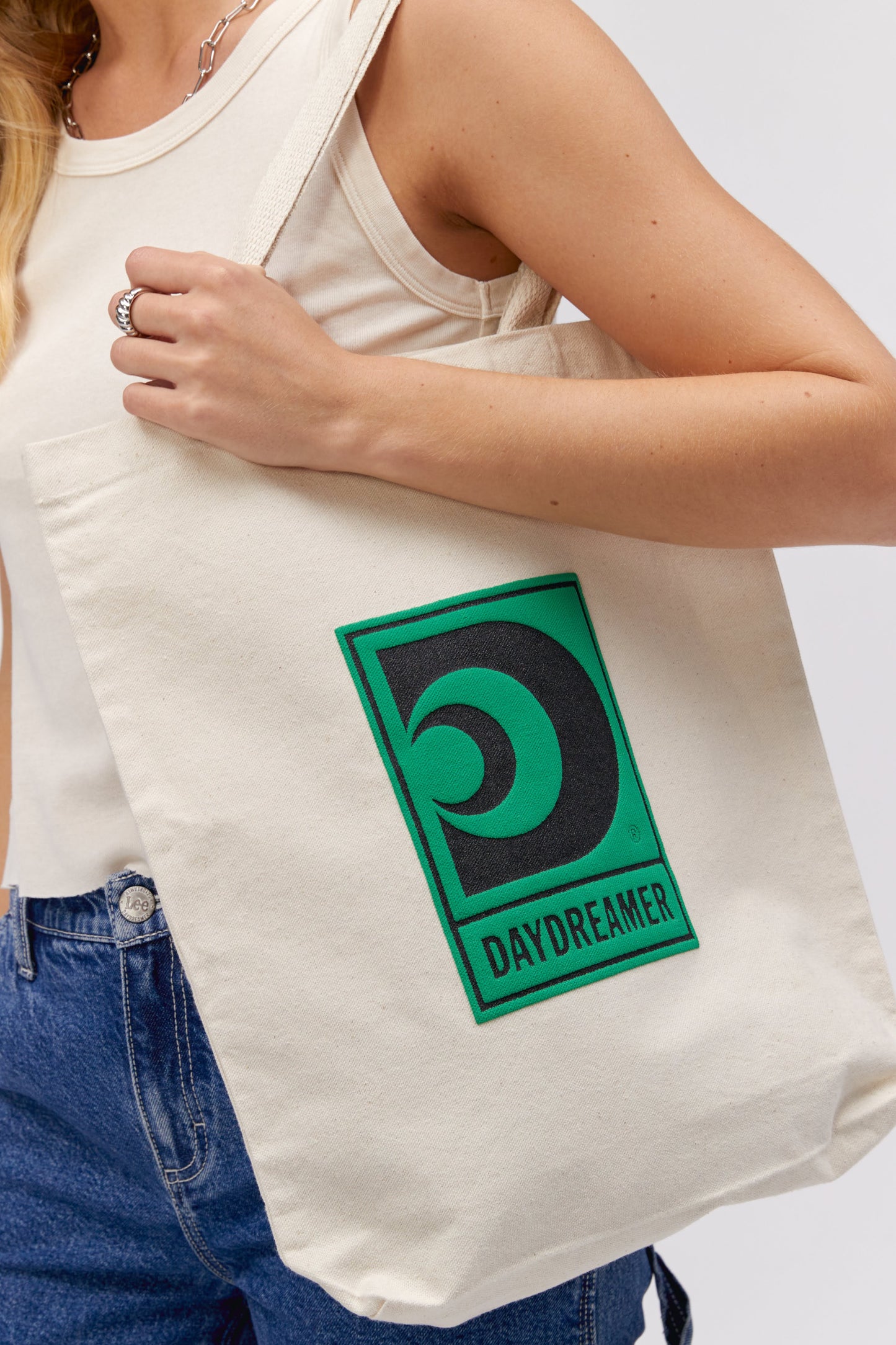 BLONDE MODEL HOLDING CANVA TOTE WITH GREEN DAYDREAMER LOGO IN CENTER
