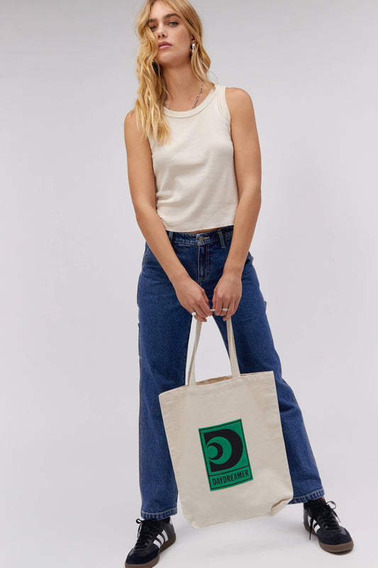 BLONDE MODEL HOLDING CANVA TOTE WITH GREEN DAYDREAMER LOGO IN CENTER