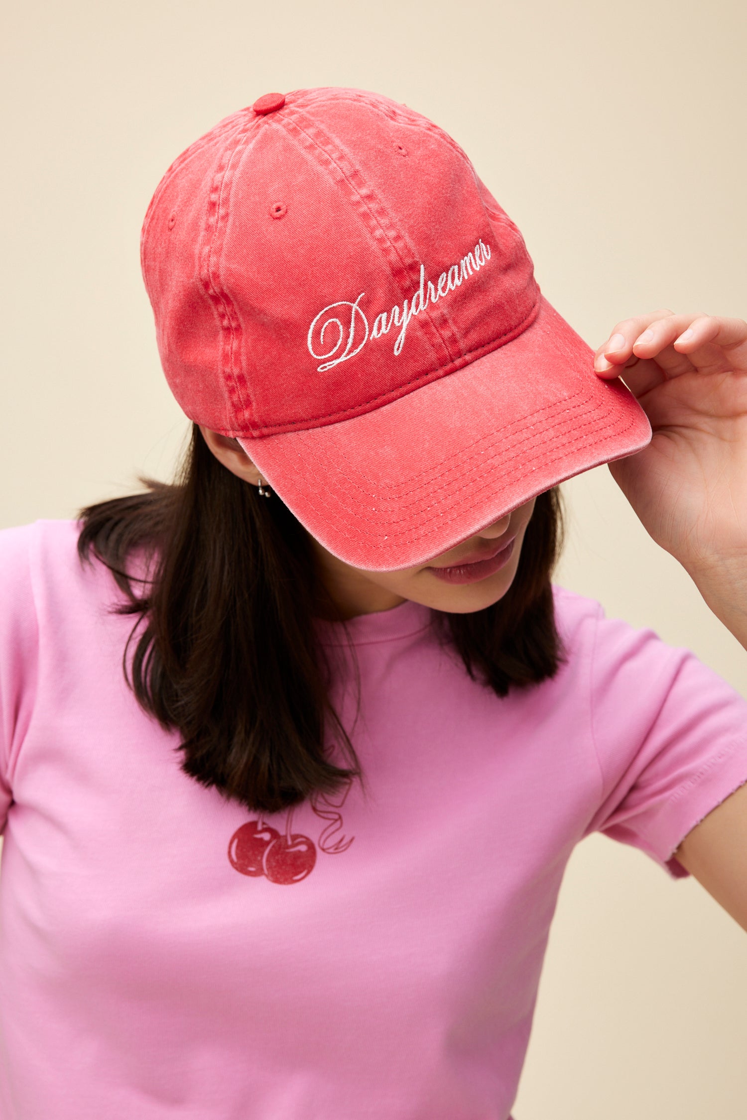 Model wearing a washed red denim dad hat with 'Daydreamer' logo script embroidered on the front.