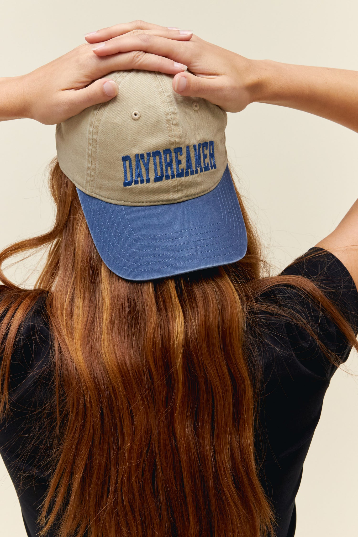 Model wearing a two-tone dad hat in blue and tan with collegiate-style 'Daydreamer' logo embroidery on the front.