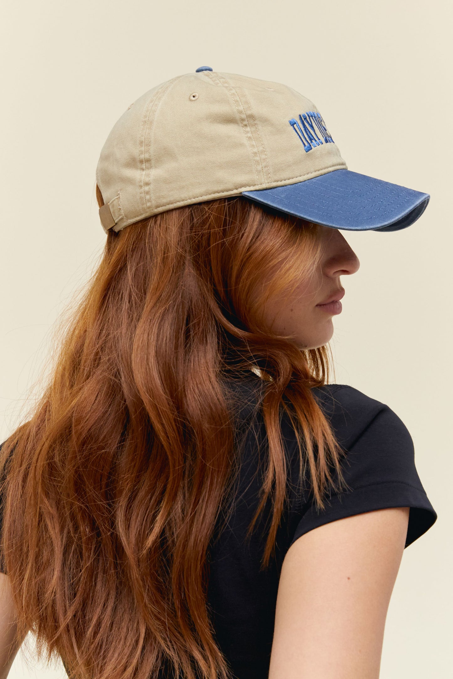 Model wearing a two-tone dad hat in blue and tan with collegiate-style 'Daydreamer' logo embroidery on the front.