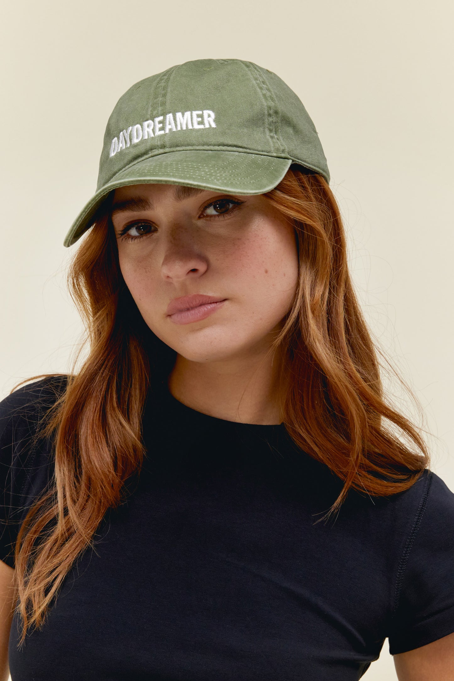 Model wearing a washed green dad hat with Daydreamer logo embroidery on the front and back.
