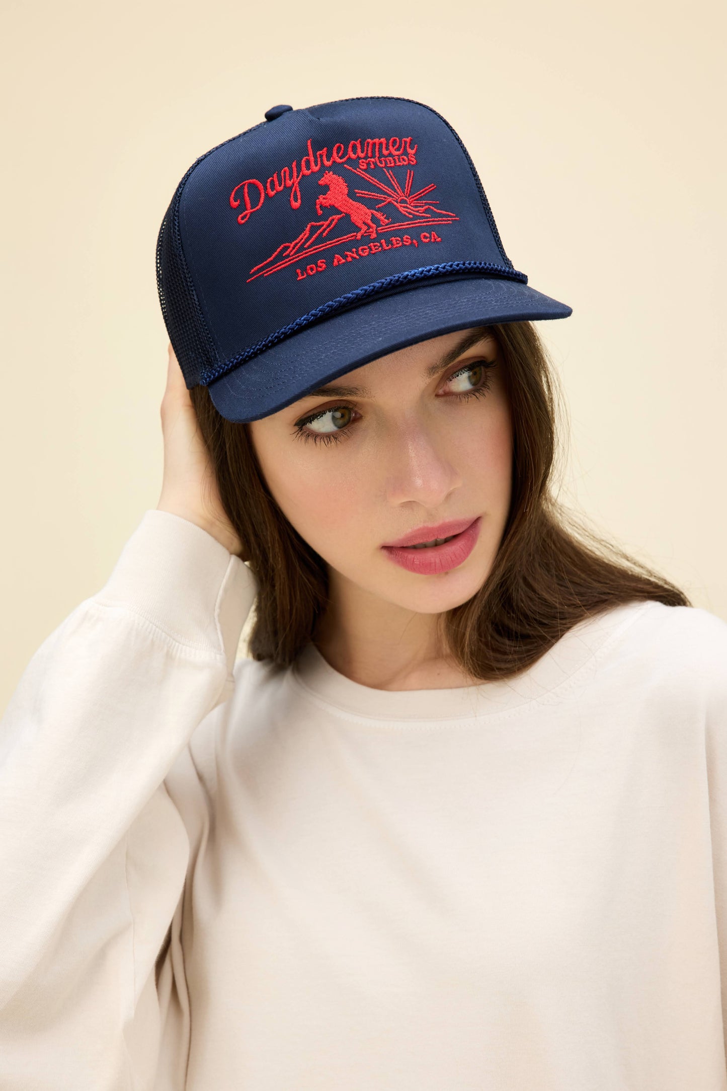 Model wearing a navy blue trucker hat with western-style 'Daydreamer Studios' embroidery on the front.
