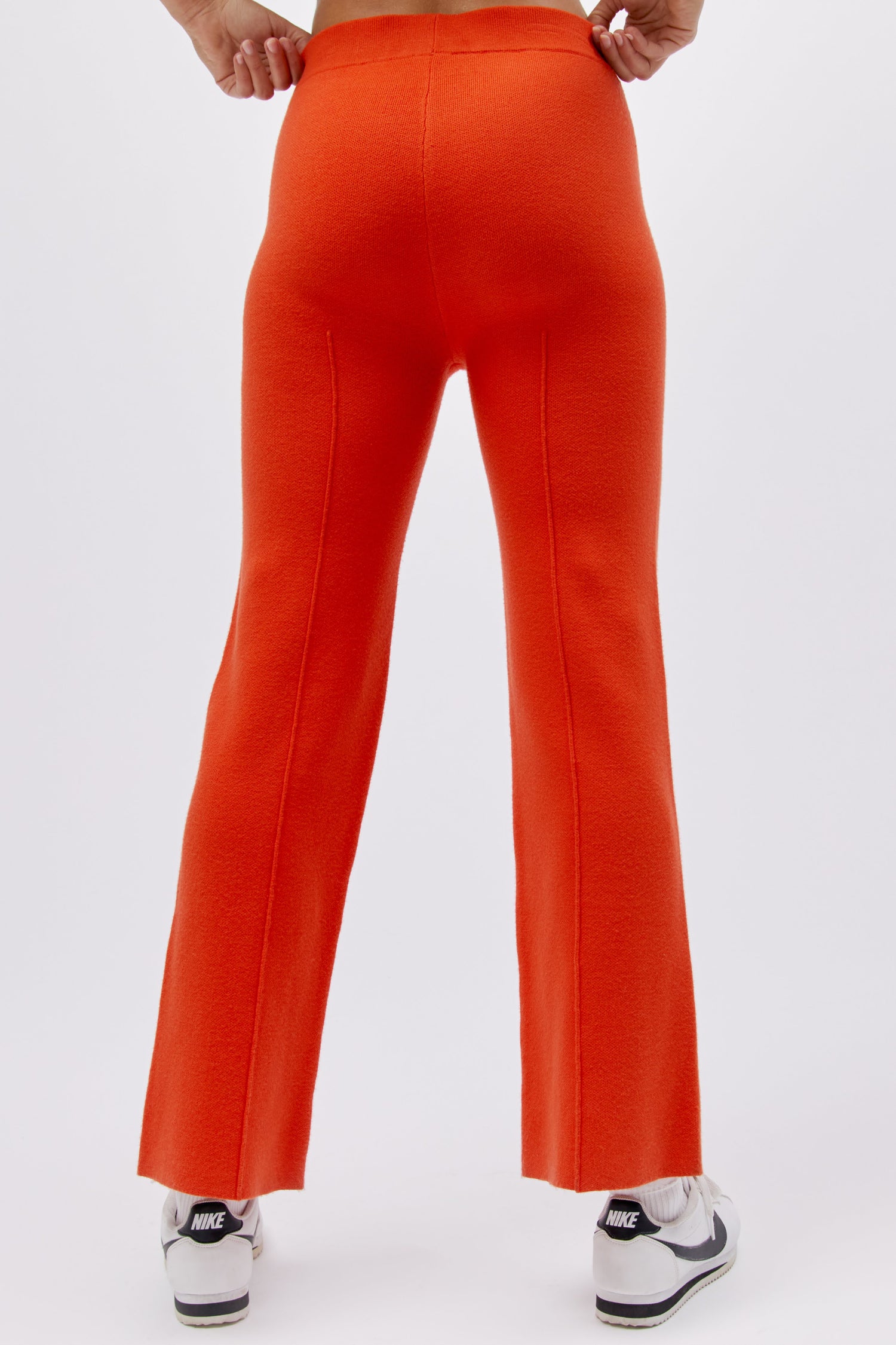 A model featuring a hot orange pintuck pant.