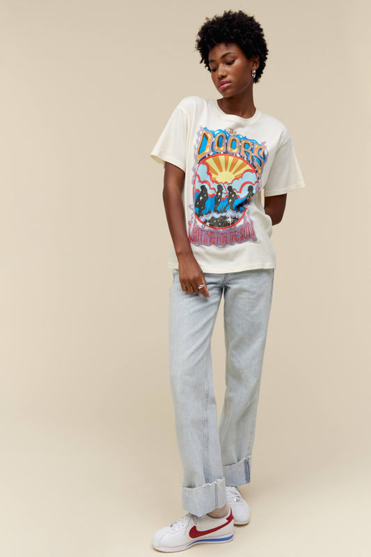 A model featuring a white tee designed with an exclusive rendition of The Door’s lead members at sunrise, inspired by the album’s original cover.