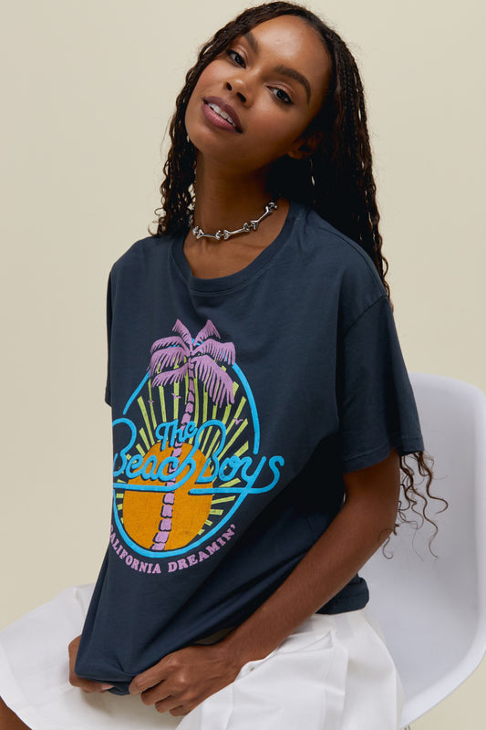 A model featuring a black tee stamped with "The Beach Boys" in front of a sun and palm tree graphic