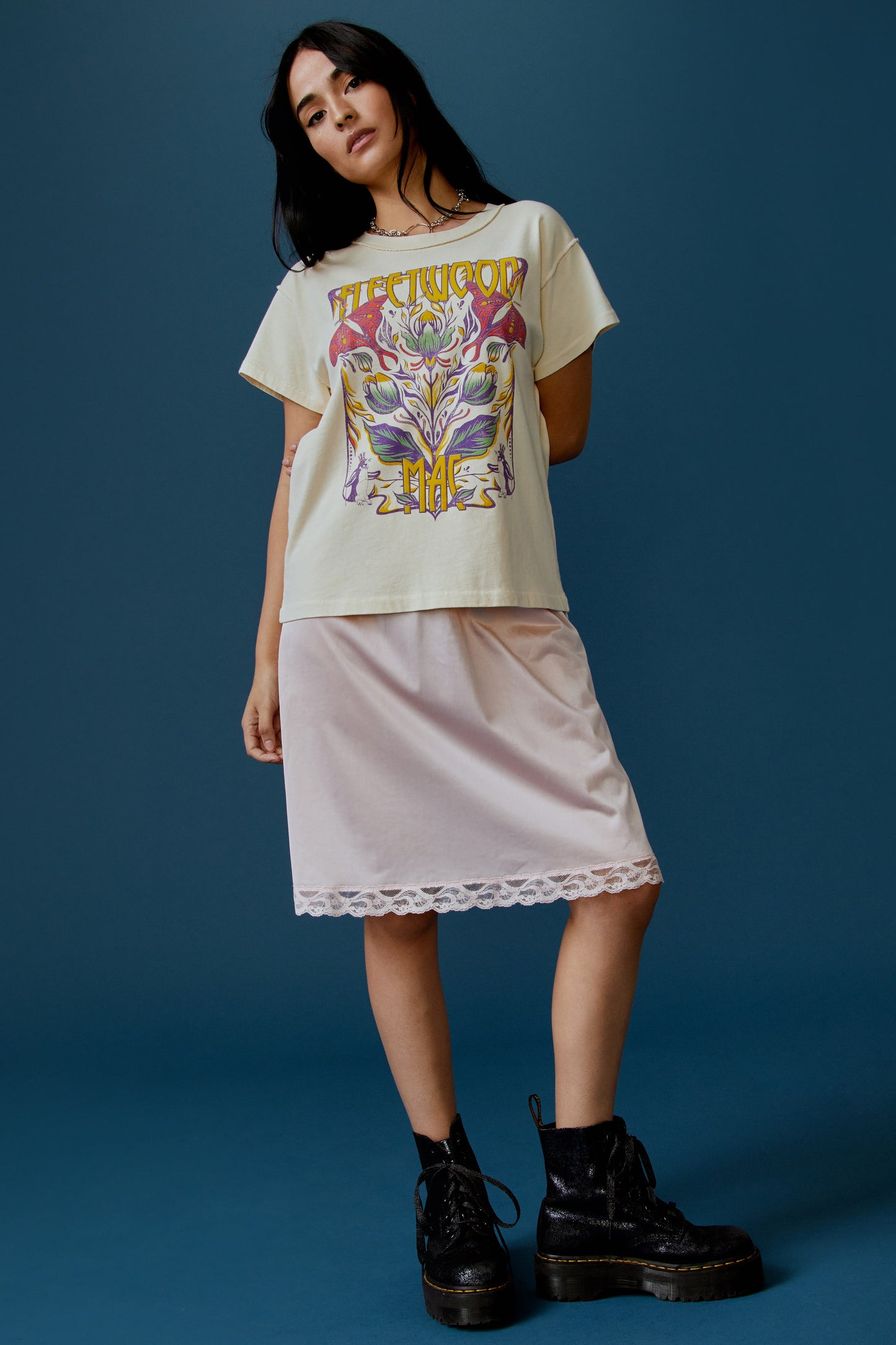 A dark-haired model featuring a parchment-colored tee stamped with the band's name, designed with a graphic of leaves, flowers, and butterflies on the center.