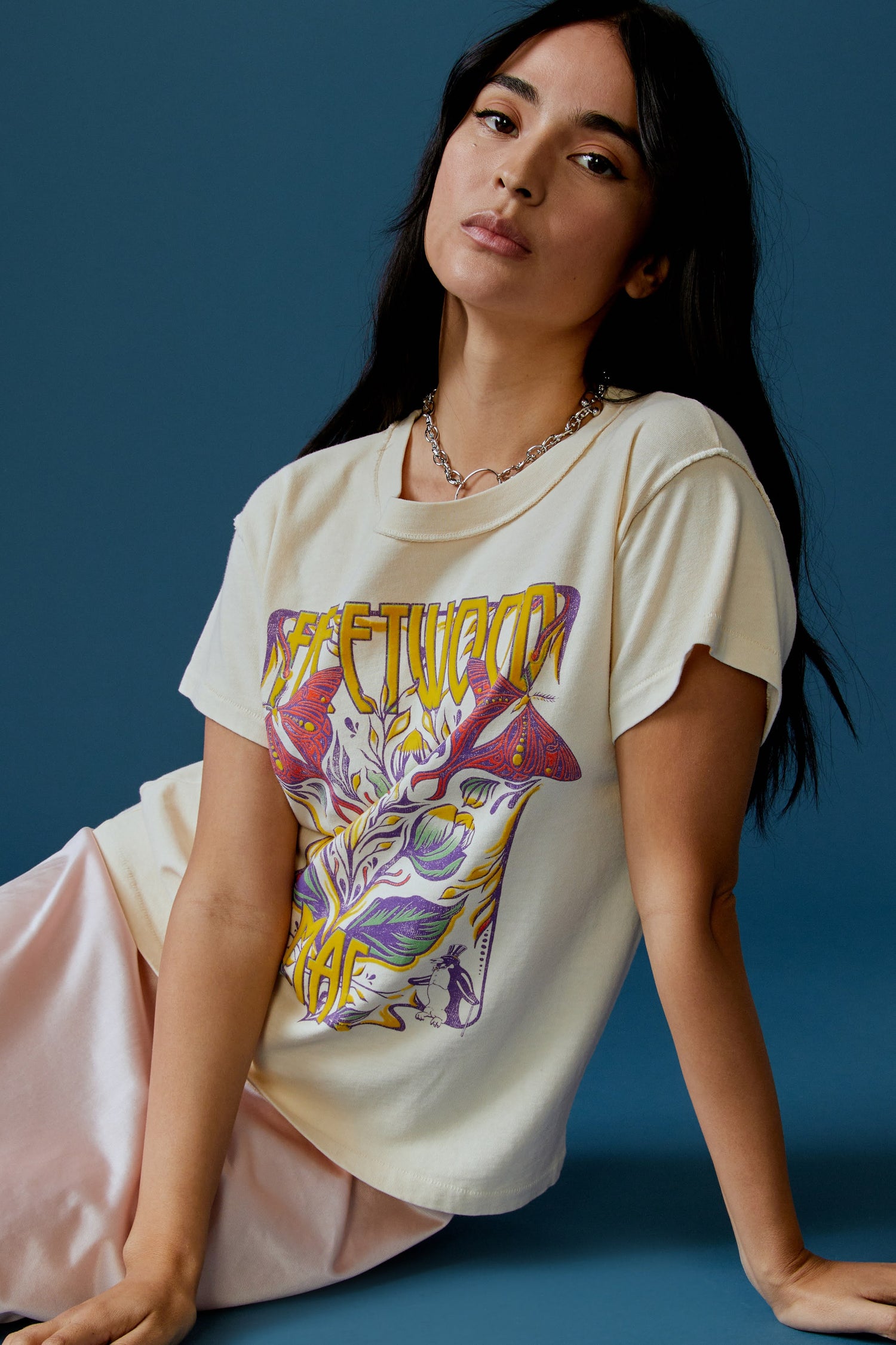 A dark-haired model featuring a parchment-colored tee stamped with the band's name, designed with a graphic of leaves, flowers, and butterflies on the center.