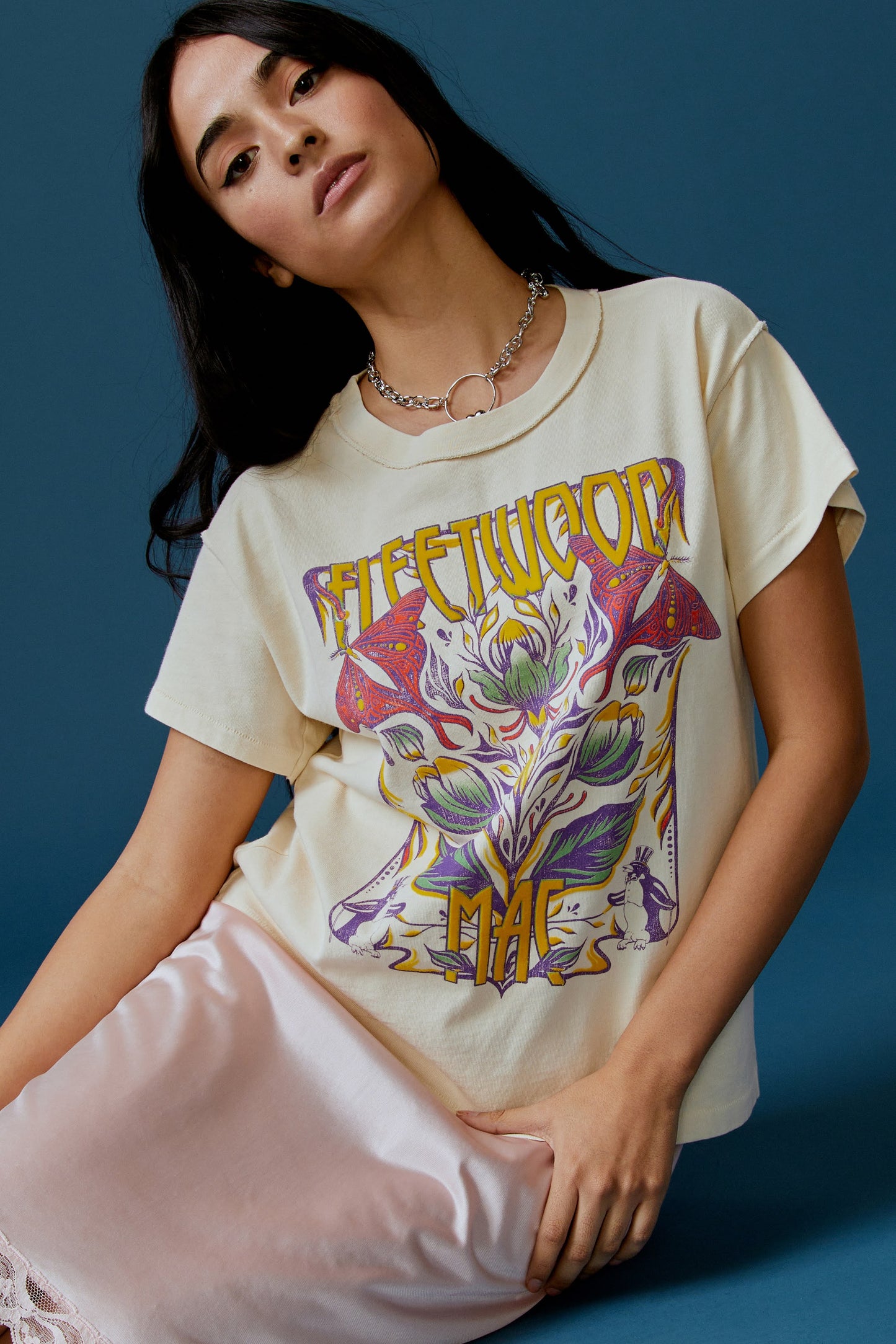 A dark-haired model featuring a parchment-colored tee stamped with the band's name, designed with a graphic of leaves, flowers, and butterflies on the center.