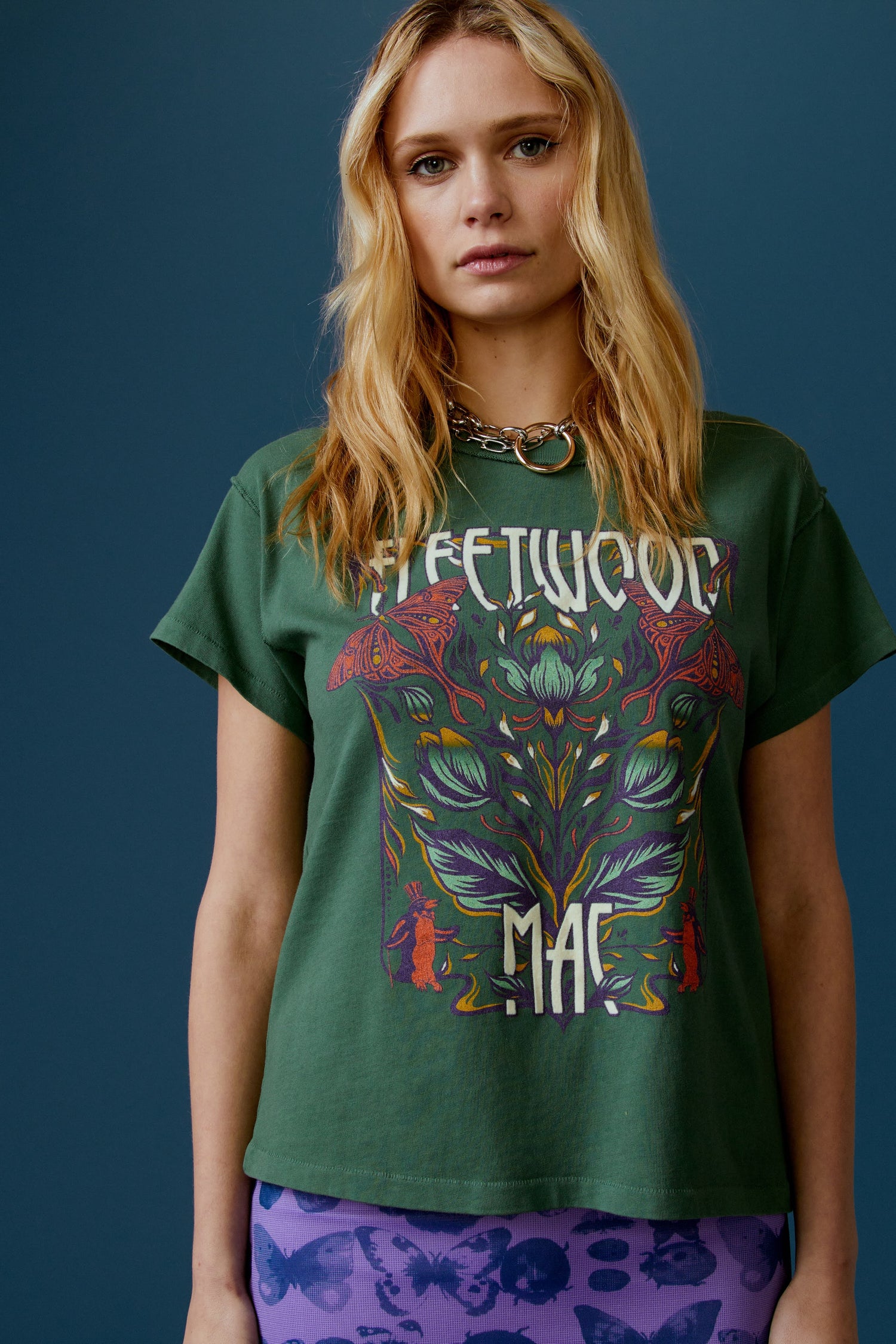A blonde-haired model featuring a stormy green tee stamped with the band's name, designed with a graphic of leaves, flowers, and butterflies on the center.