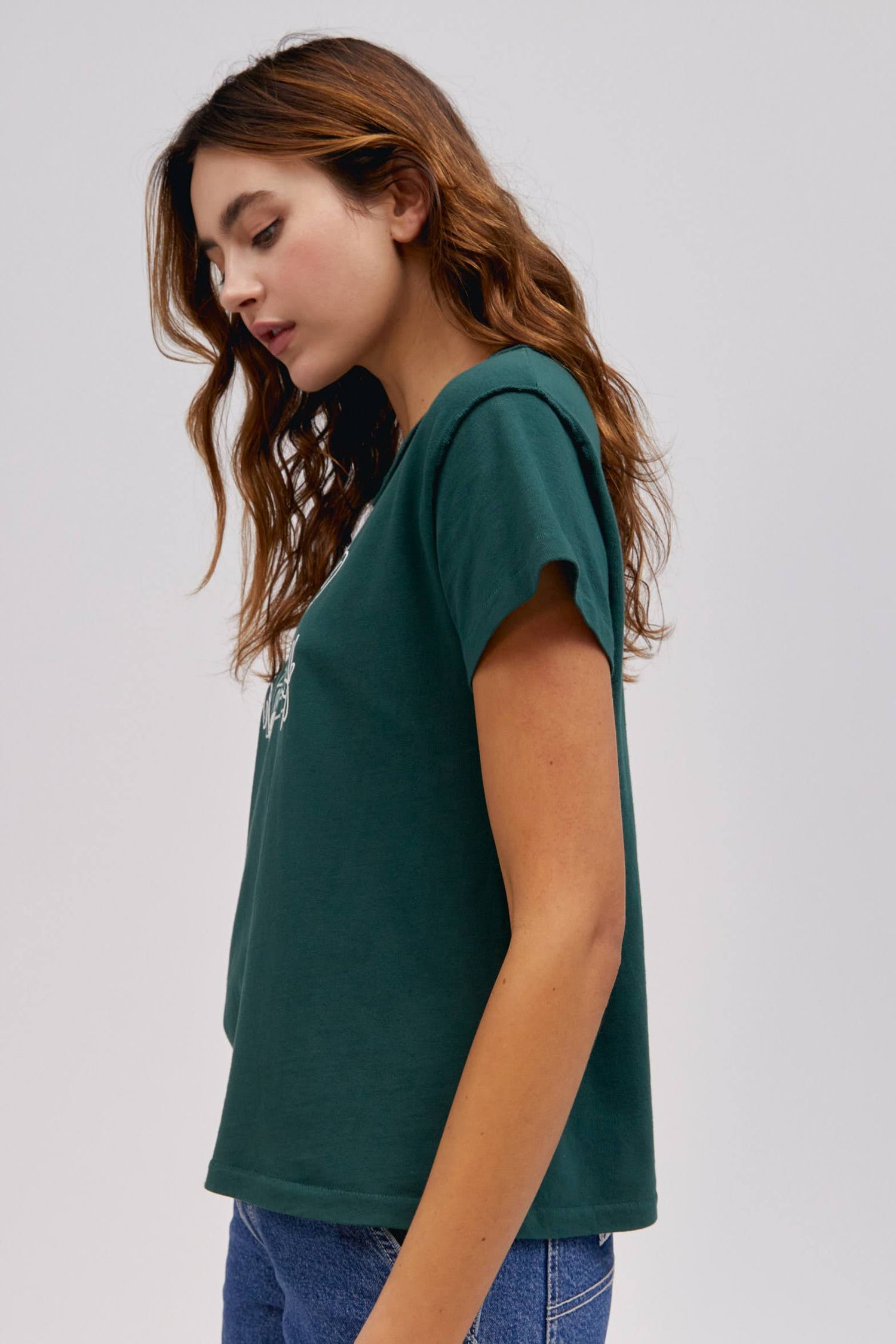 A curly-haired model featuring a pine reverse gf tee designed with the original Lee workwear logo reimagined into an exclusive, co-branded graphic with layered doodles in puff ink.