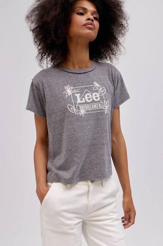 A curly-haired model featuring a heather grey reverse gf tee designed with the original Lee workwear logo reimagined into an exclusive, co-branded graphic with layered doodles in puff ink.