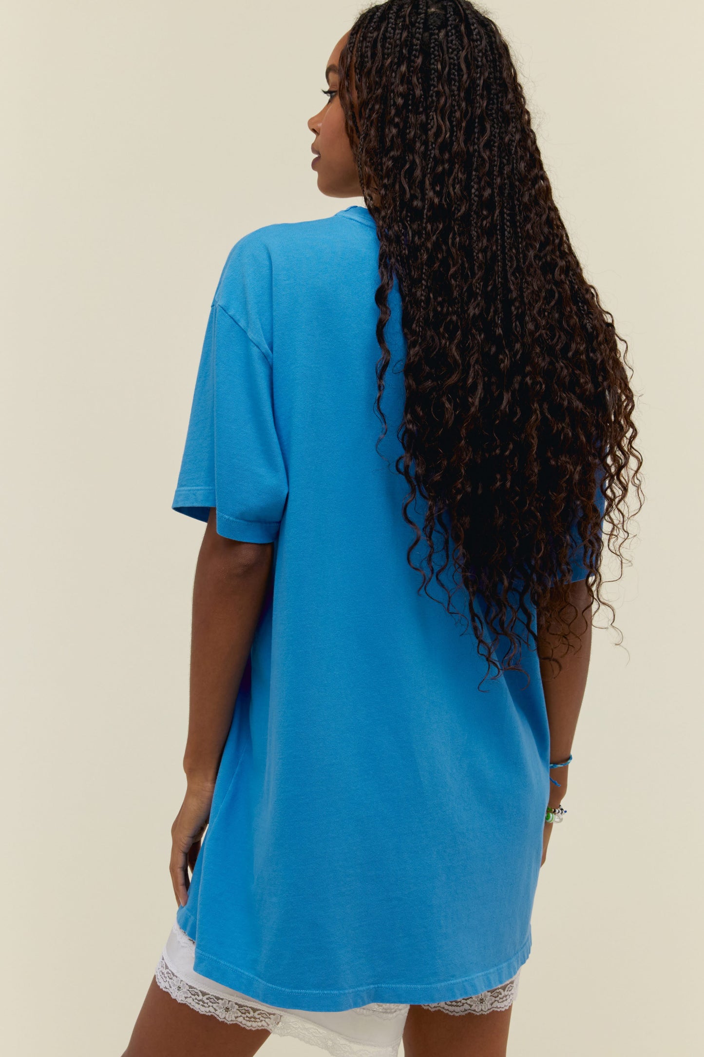 A dark-haired model featuring a blue t-shirt dress stamped with "Fleetwood Mac Rumours" on top centered with the graphic design of the same album art
