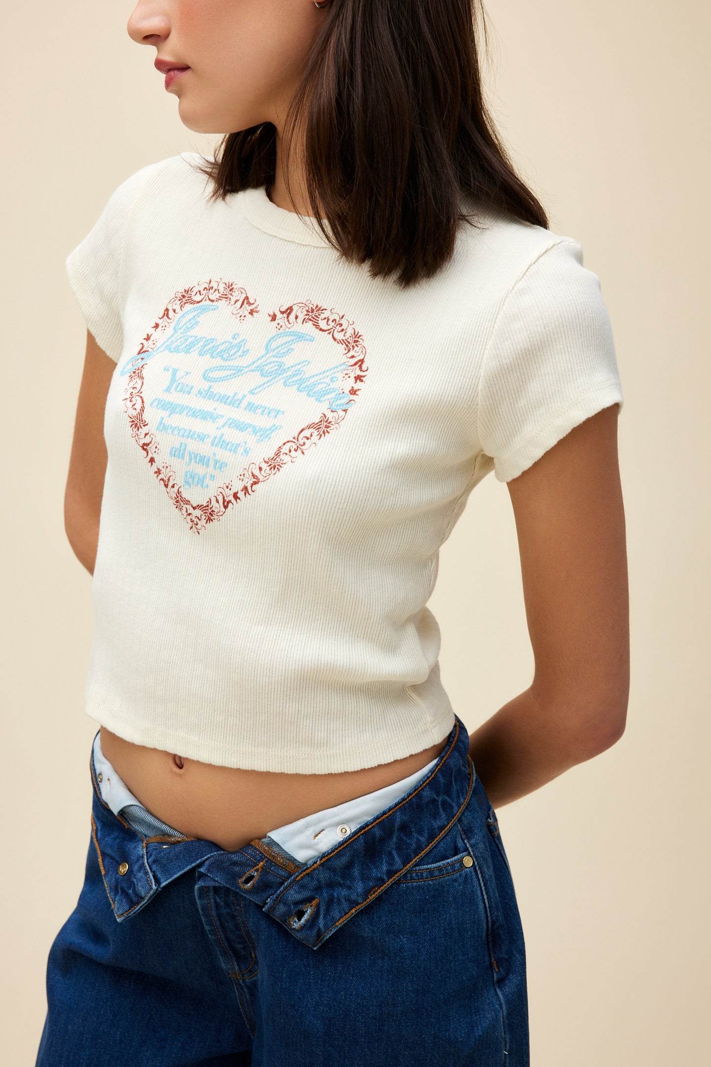 A model featuring a stone vintage baby tee featuring a red lace heart with Janis Joplin’s legendary ‘never compromise’ quote written in blue on the center. 