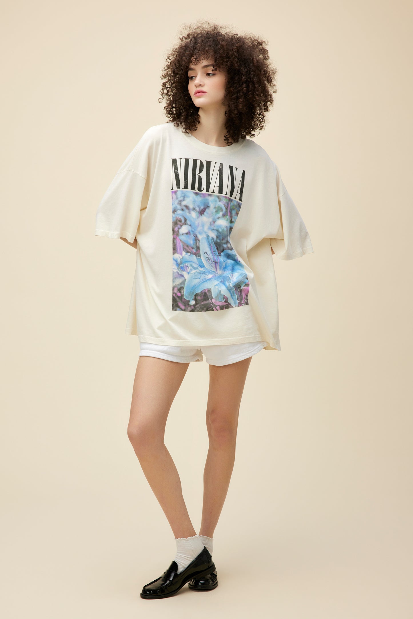 A model featuring a cream tee designed with a lily graphic and "Nirvana" in the center.