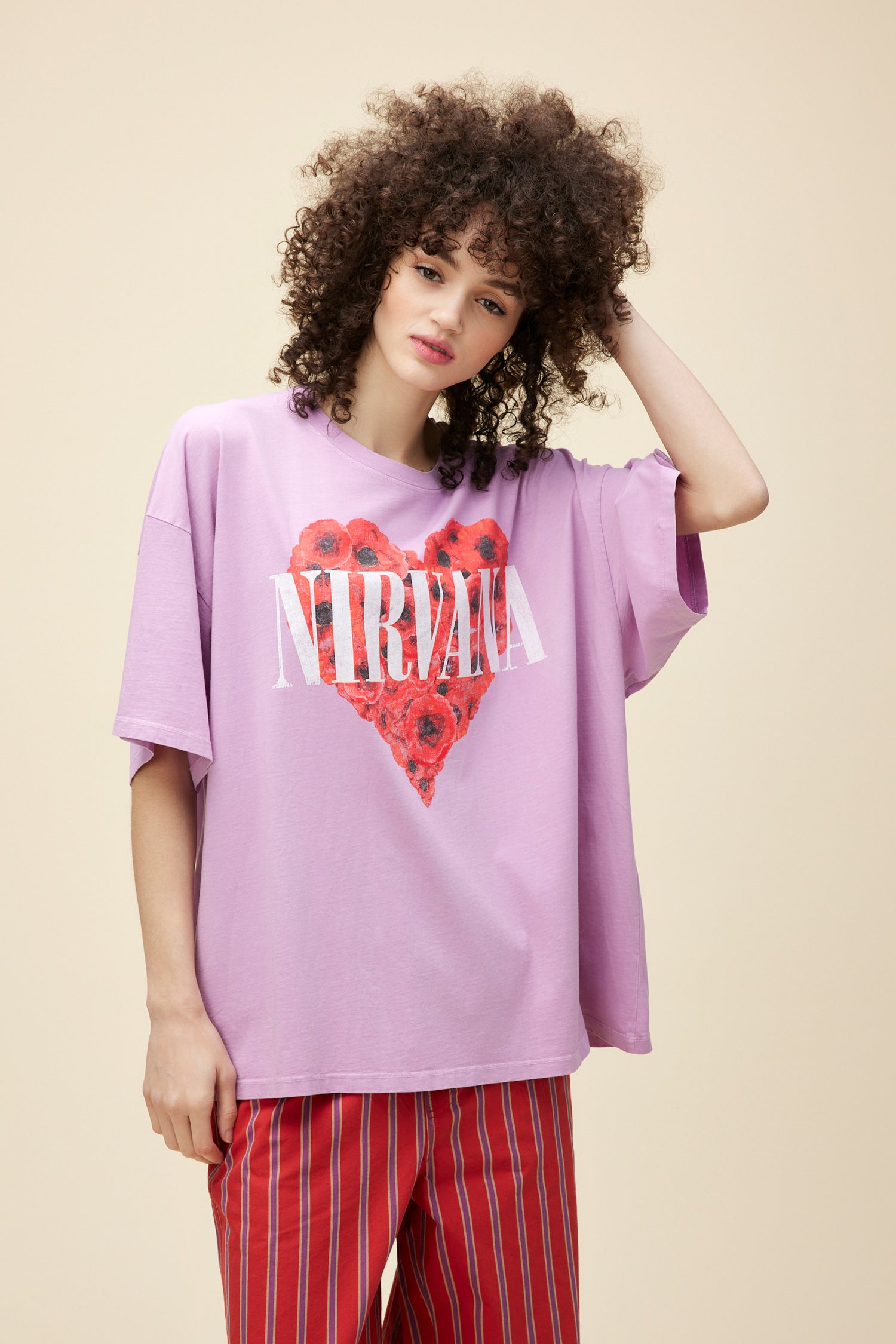 A model featuring a violet tee designed with an original graphic featuring a heart full of roses lands center stamped with both 'Nirvana' and the track's name.