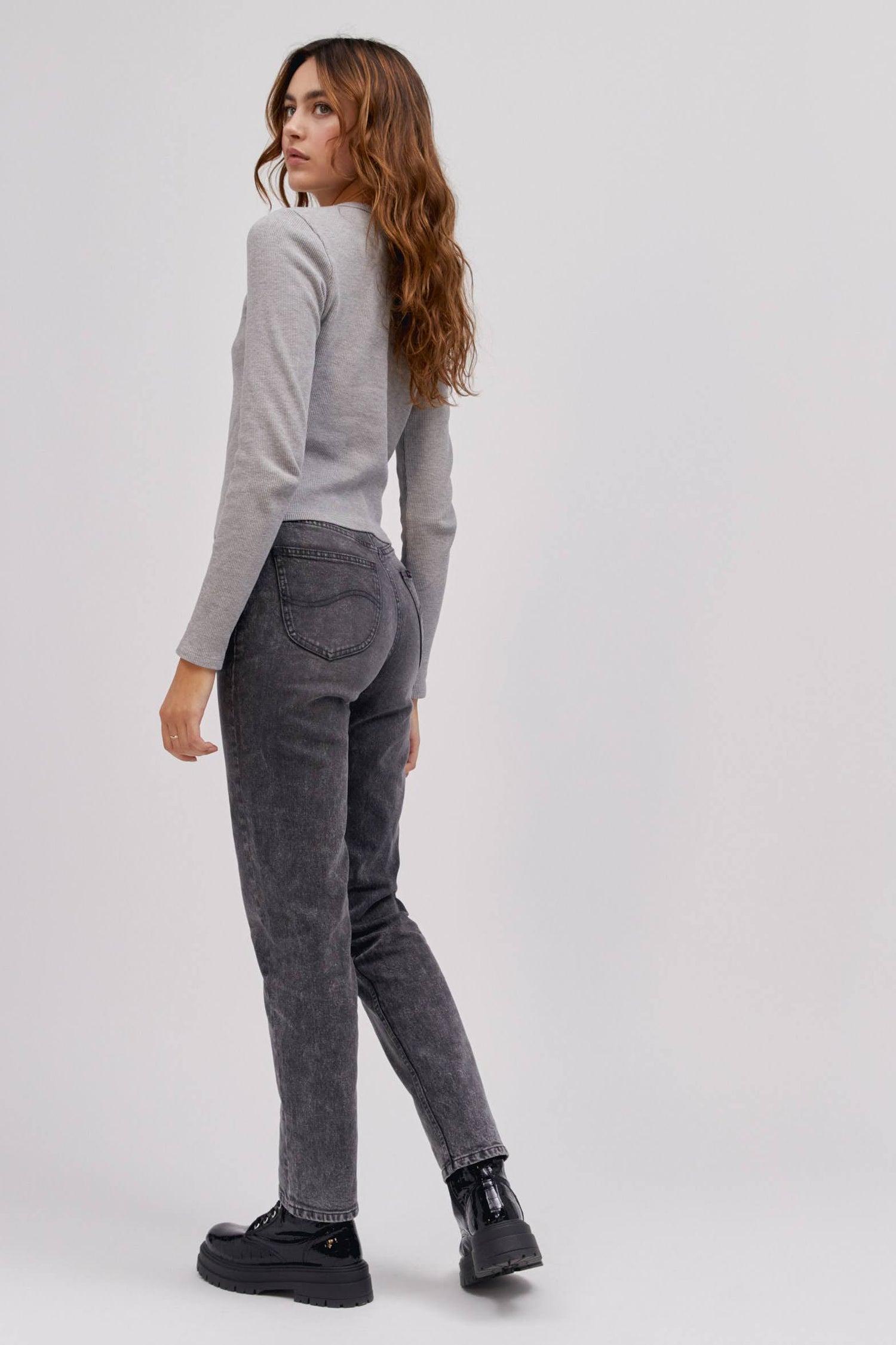 A curly-haired model featuring a grey classic lightweight thermal with a sharp turn colored high rise and straight-legged jeans with a slim fit through the hips.