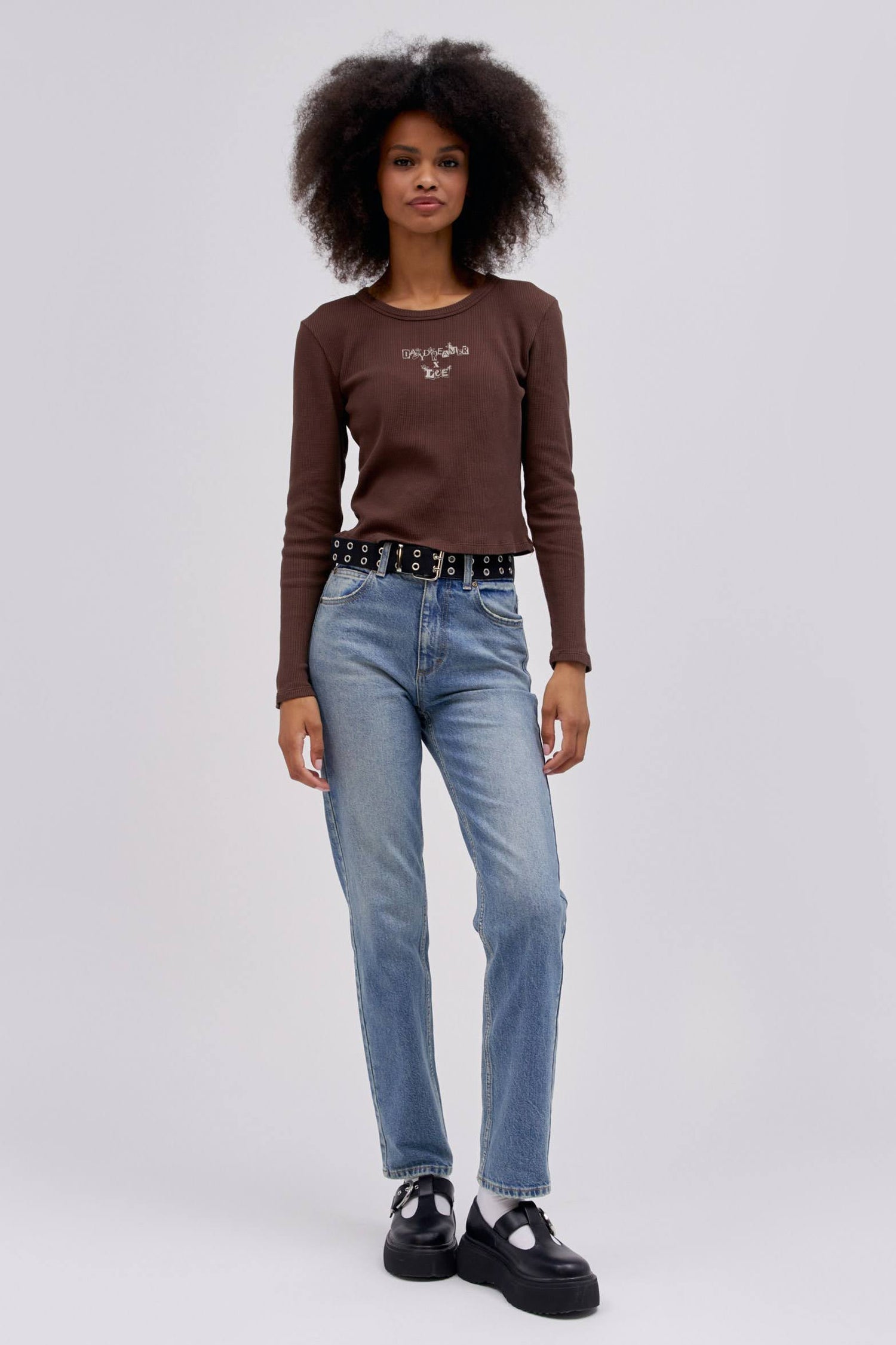 A curly-haired model featuring a dark brown classic lightweight thermal with a mid storm colored high rise and straight-legged jeans with a slim fit through the hips.