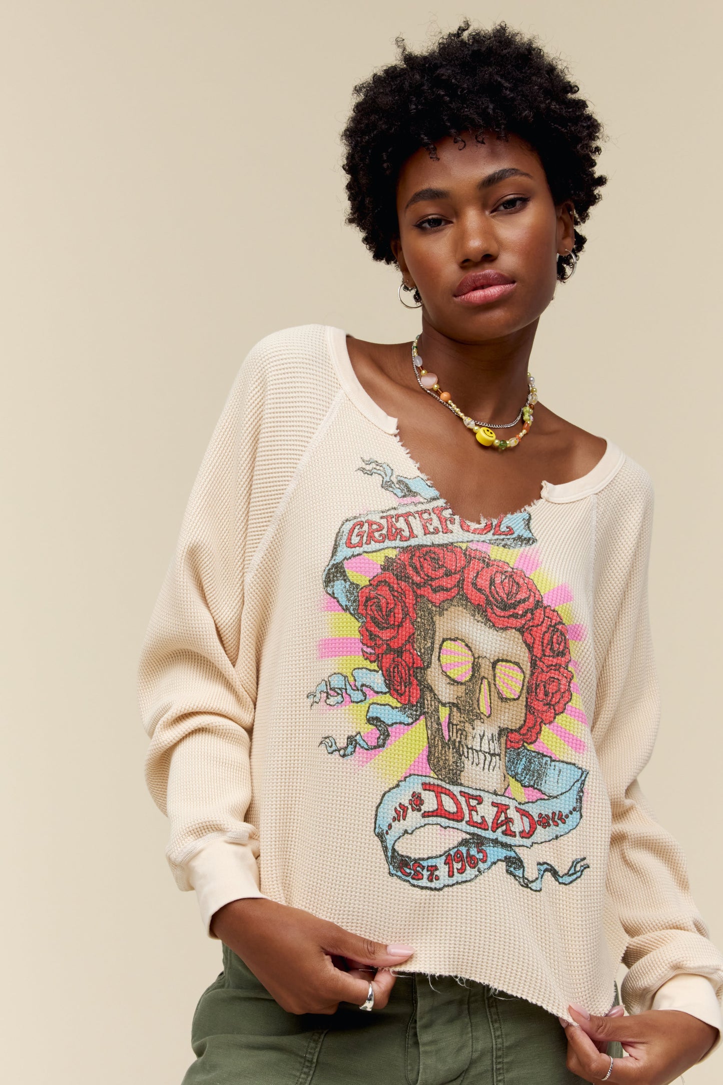 A model featuring a sand vcut long sleeve designed with a graphic of a skull and stamped with grateful dead in red font.