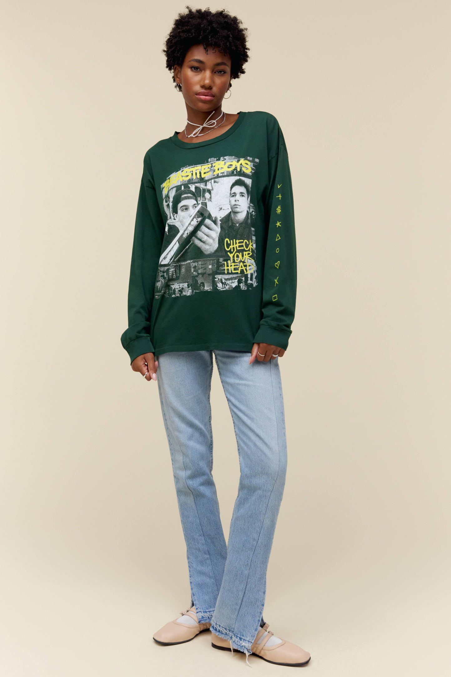 A model featuring a vintage green Beastie Boys long sleeve designed with the album title and a scanned looking collage of multiple photos of the boys and their history, with hand drawn symbols down the left sleeve.