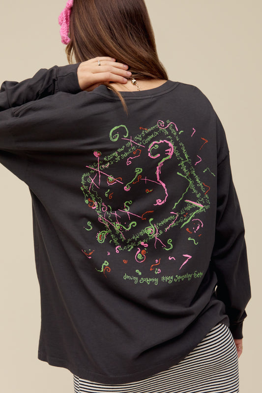 A model featuring a black The Cure long sleeve merch designed with a hand-drawn portrait of Smith and doodles in puff ink and pops of color.