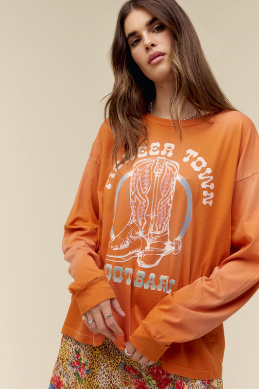 A model featuring a tangerine colored long sleeve merch stamped with "Pioneer Town" and an authentic, quality boot lands center chest.