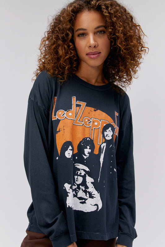 A curly-haired model featuring a black long sleeve stamped with 'Led Zeppelin' in orange, bold letters, and a portrait of each member of the band.
