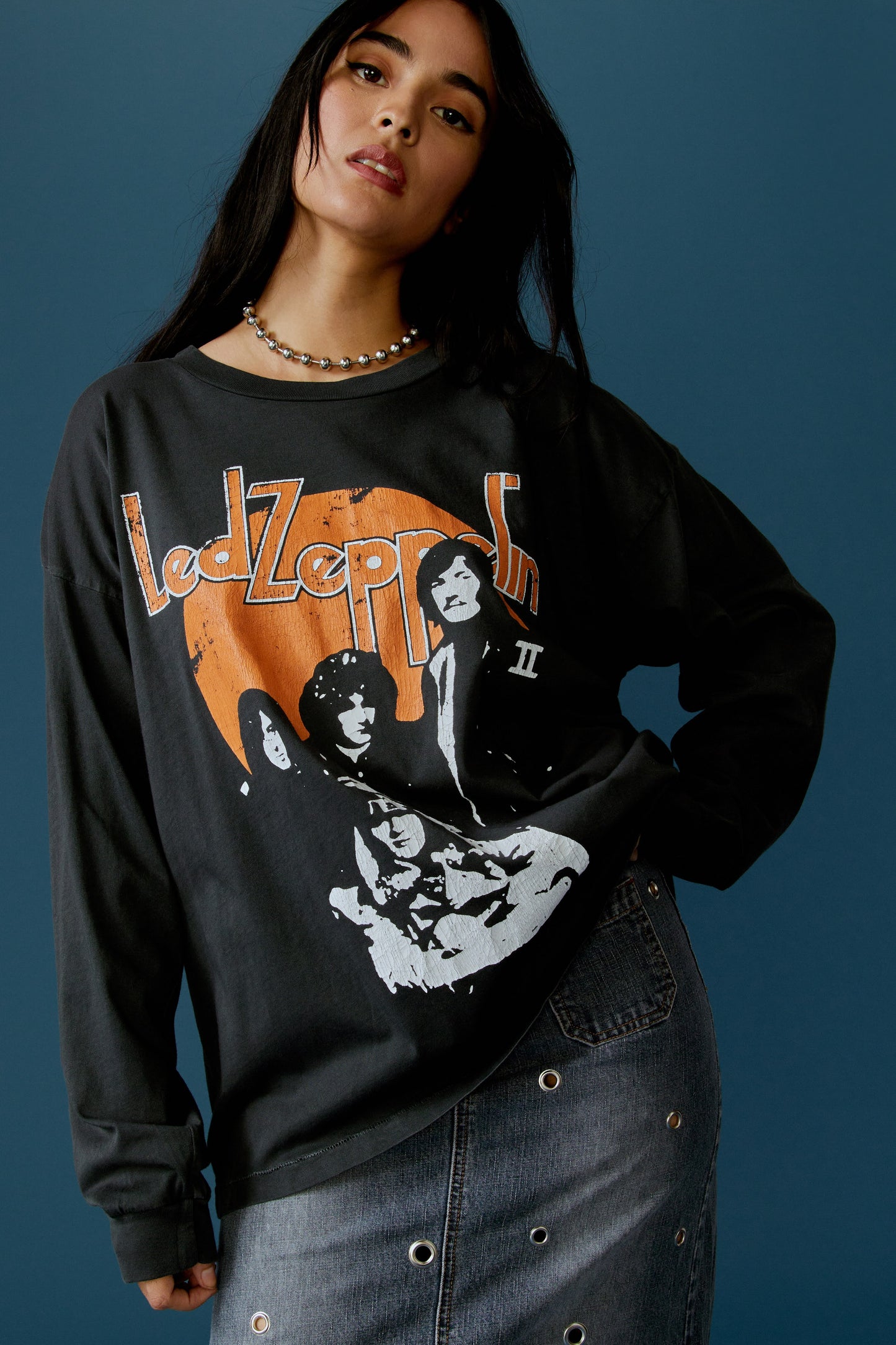 A dark-haired model featuring a black long sleeve stamped with 'Led Zeppelin' in orange, bold letters, and a portrait of each member of the band.